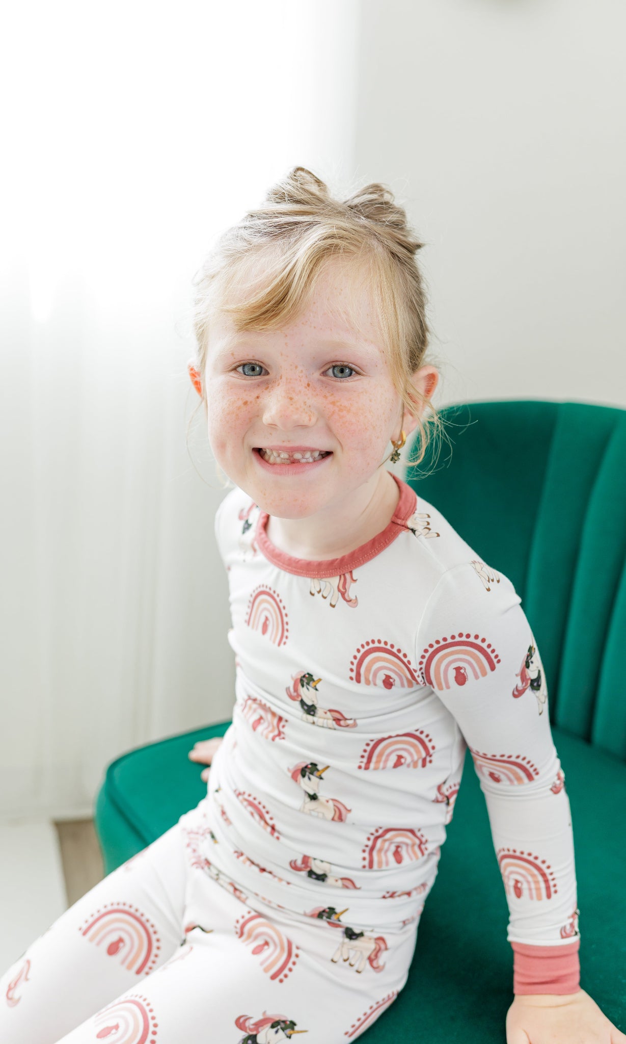 Child wearing pajamas with a pattern of owls, rainbows, and stars, sitting on a green chair.