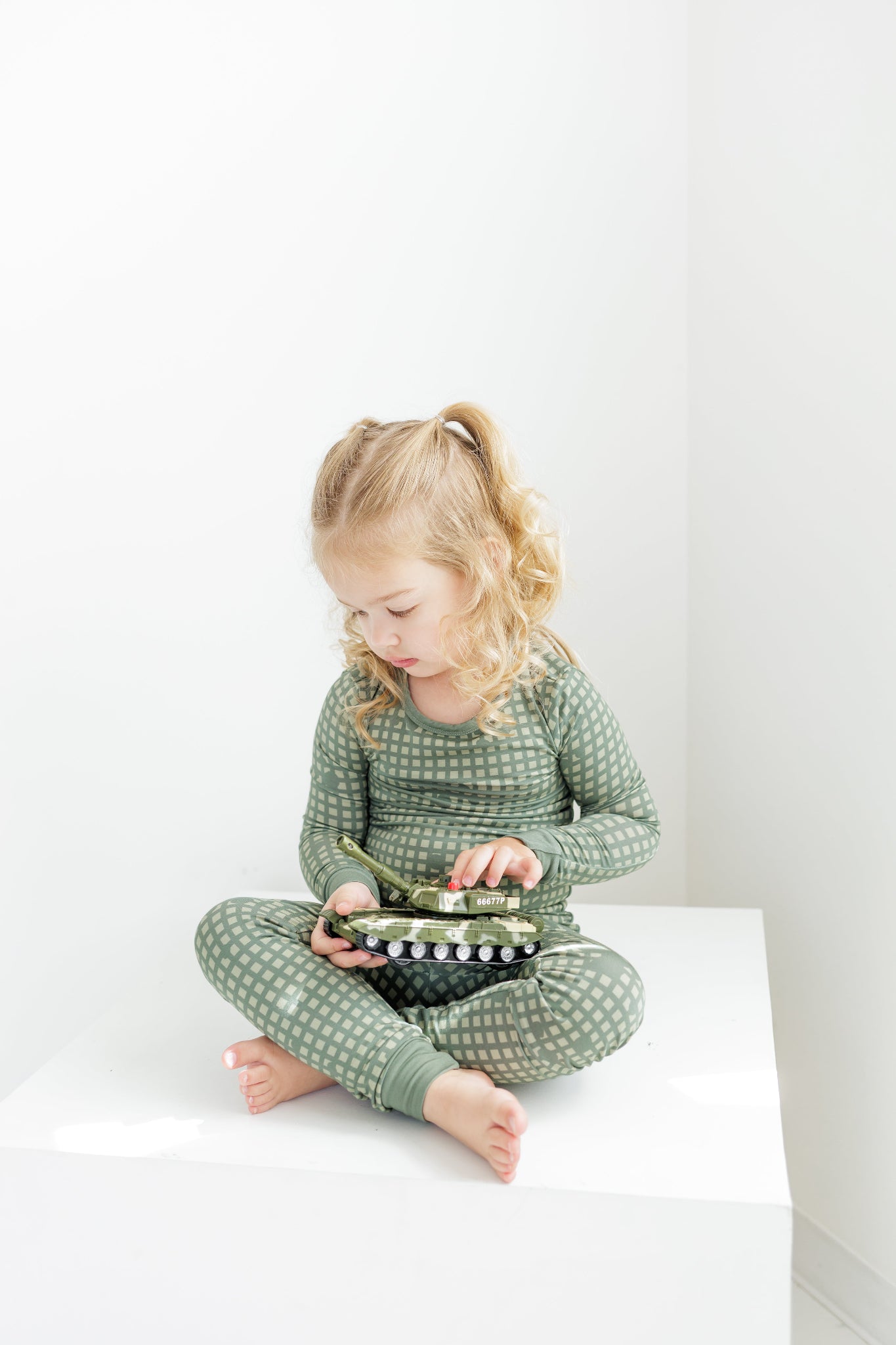 Child wearing green pajamas sitting on a white surface with a white background