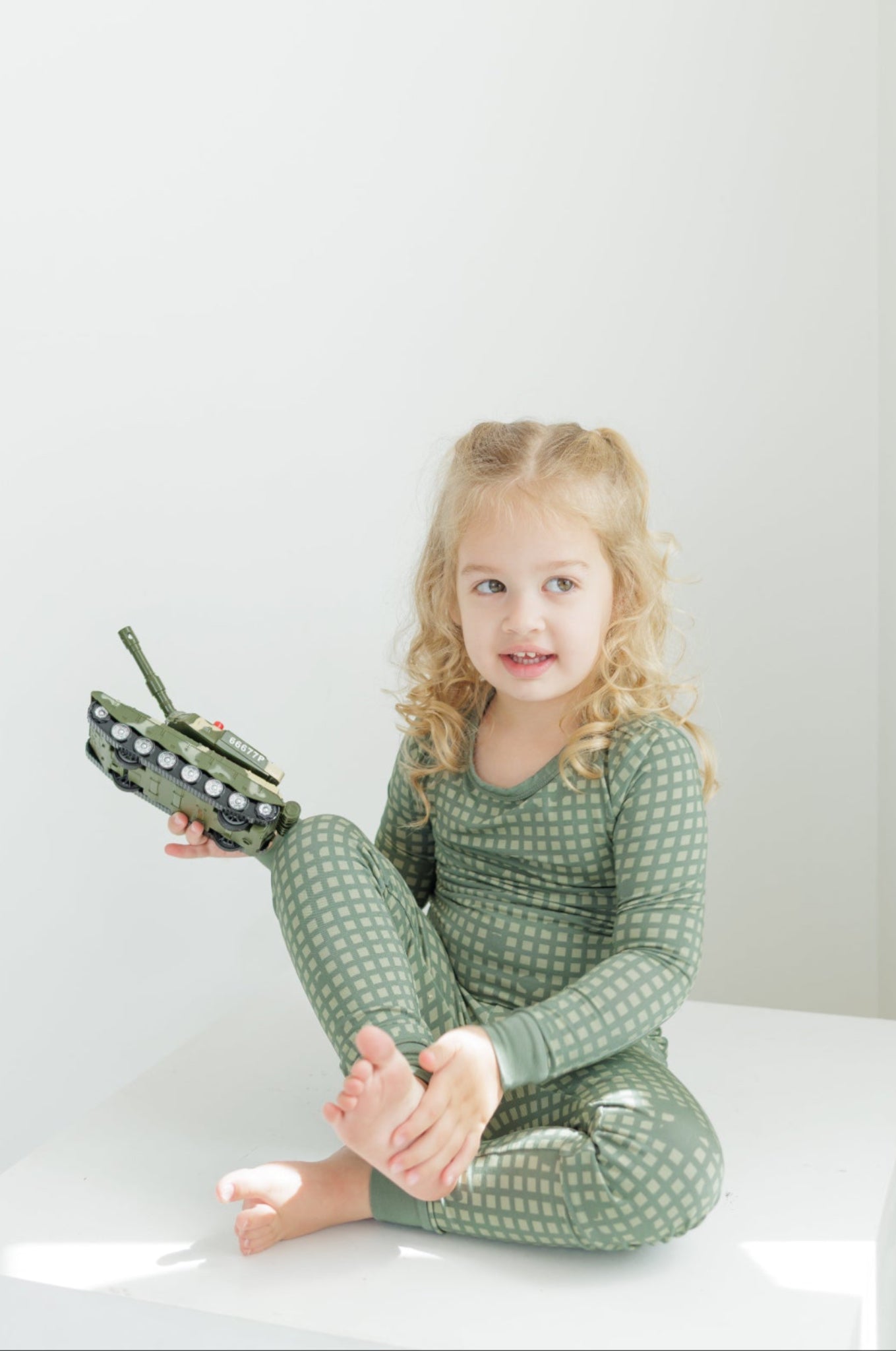 Young girl in green pajamas holding a toy on a white background