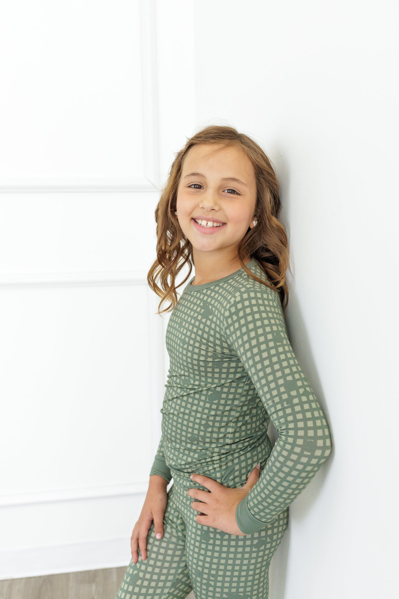 Young girl wearing a green patterned outfit against a white wall