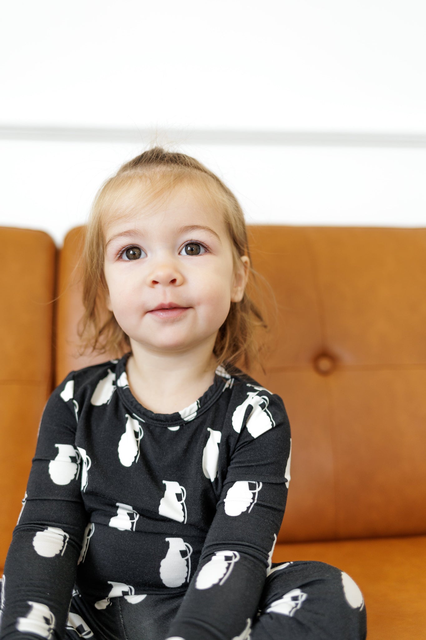 Child wearing a black outfit with white patterns sitting on a brown couch.