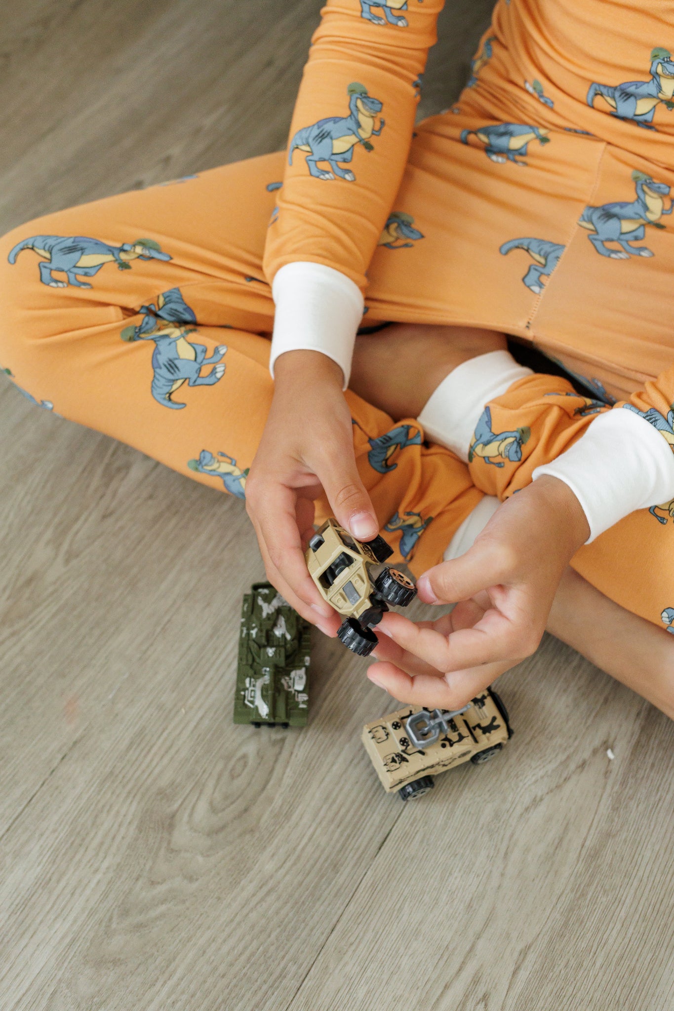 Person in orange dinosaur-patterned outfit playing with toy cars on a wooden floor