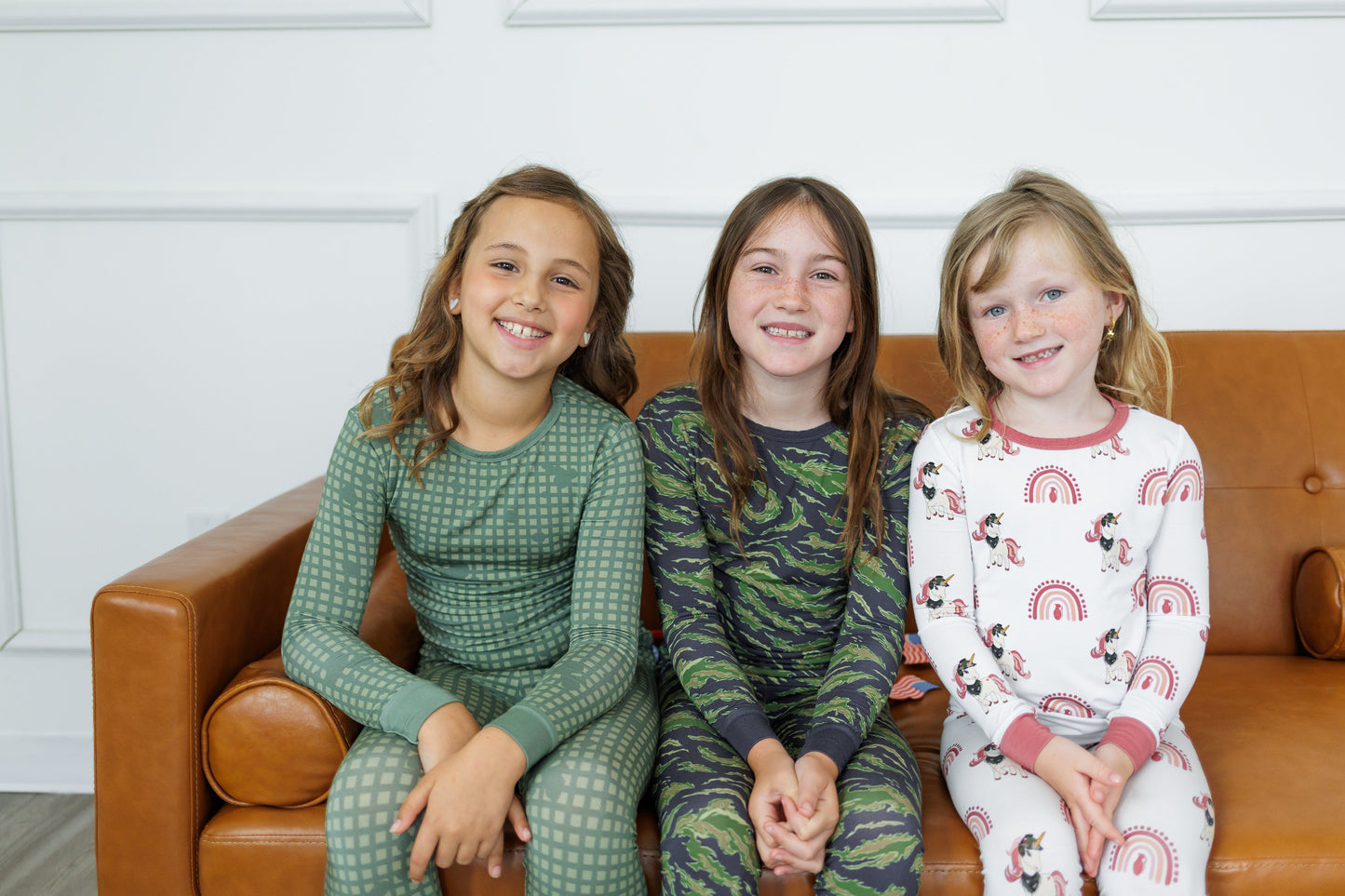 Three children sitting on a brown couch wearing pajamas.