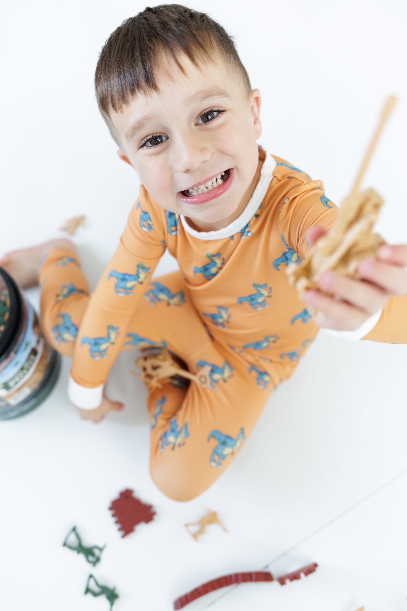Child in orange pajama with animal pattern holding a toy airplane on a white background