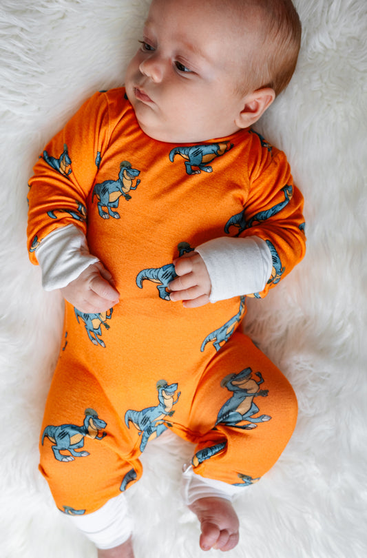 Baby wearing an orange onesie with dinosaur patterns on a white fluffy surface