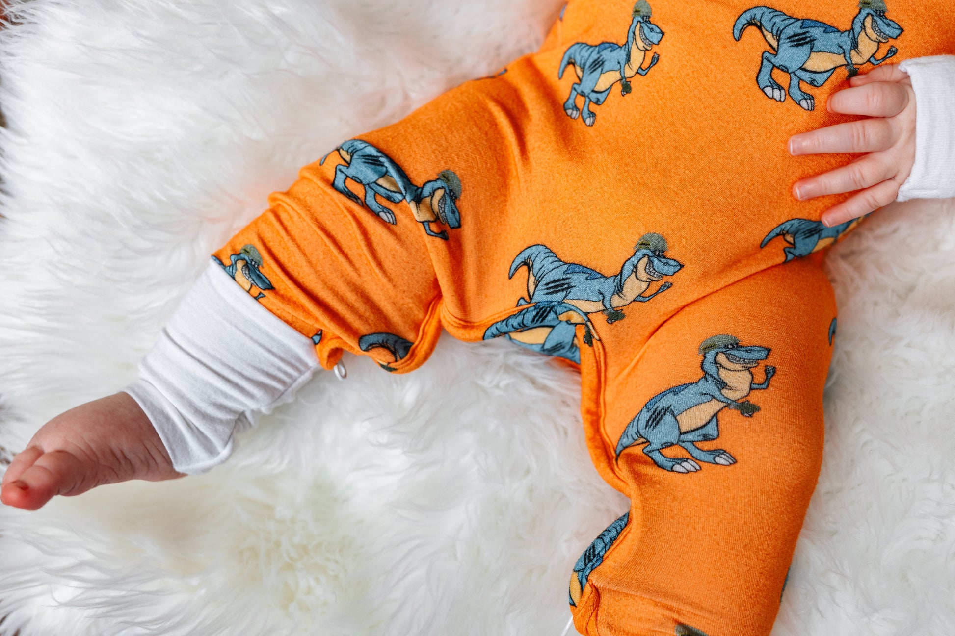 Orange baby onesie with dinosaur pattern on a white fluffy surface