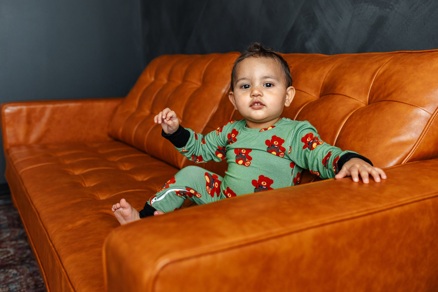 Child in a green floral outfit sitting on an orange couch.