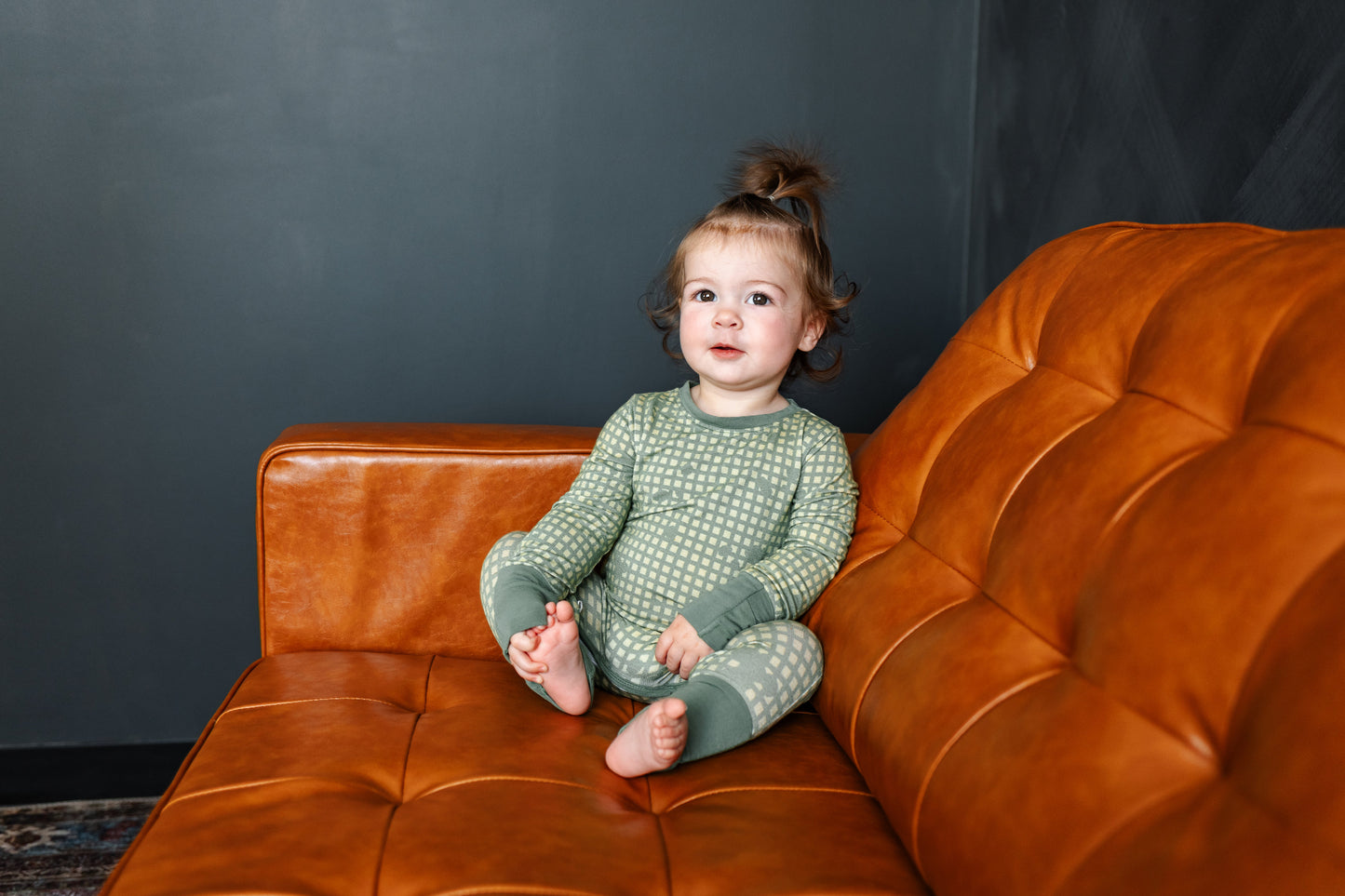 Child sitting on a brown leather couch against a dark gray wall