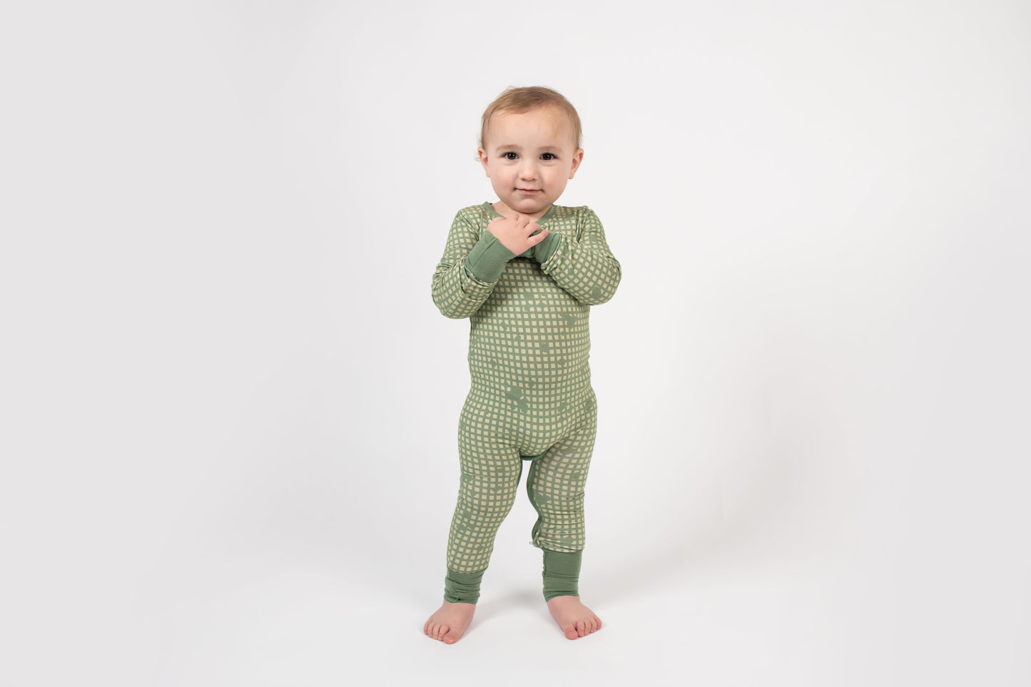 Toddler standing on a white backdrop, wearing a sage green romper with a light tan grid pattern and matching green cuffs from 3rd Coast Limited