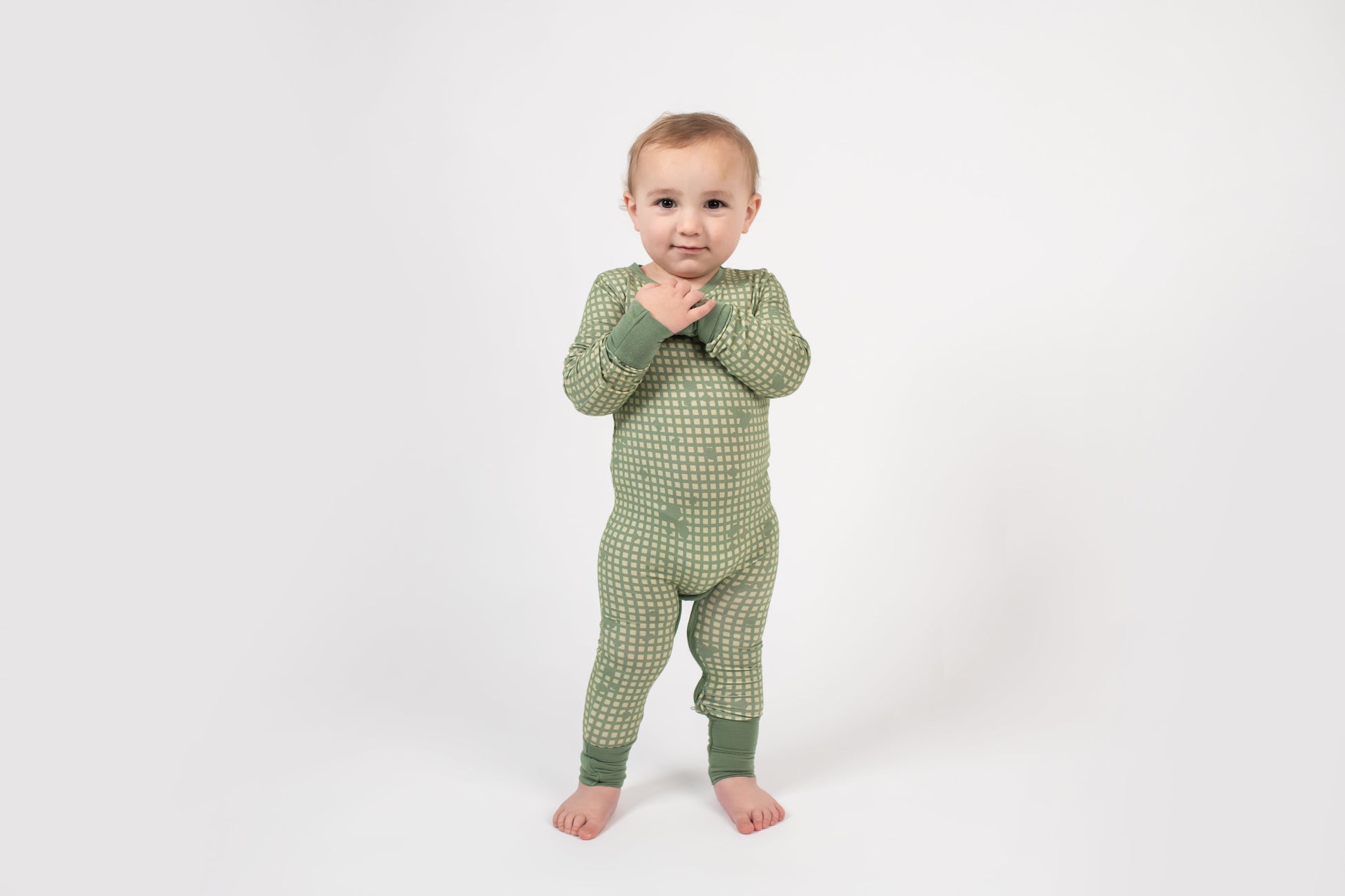 Toddler standing on a white backdrop, wearing a sage green romper with a light tan grid pattern and matching green cuffs from 3rd Coast Limited