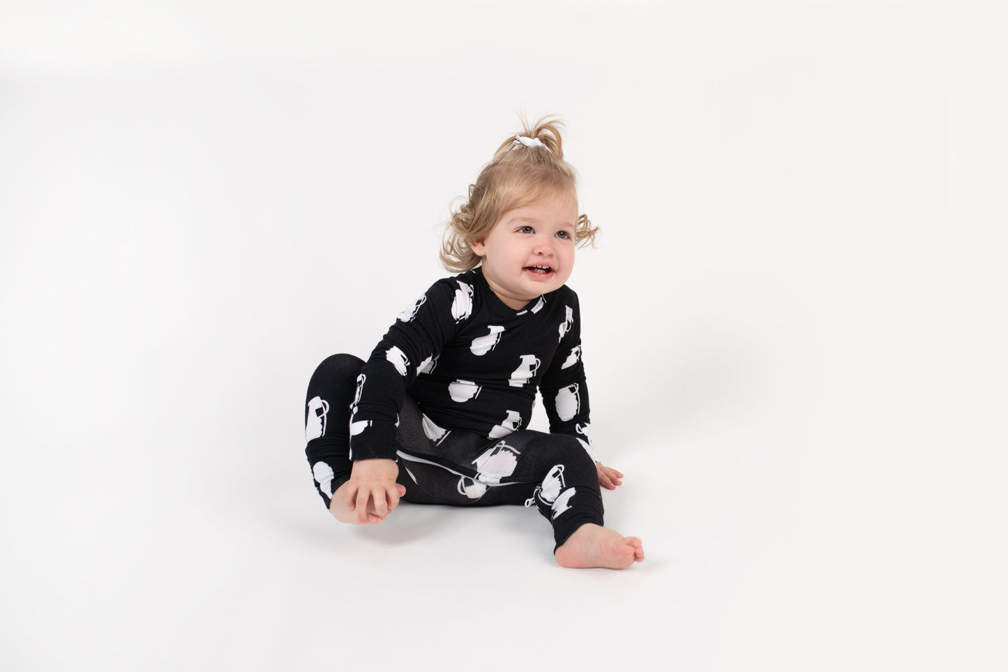 Smiling toddler sitting on a white backdrop, wearing a black long-sleeve romper with a white grenade pattern from 3rd Coast Limited.