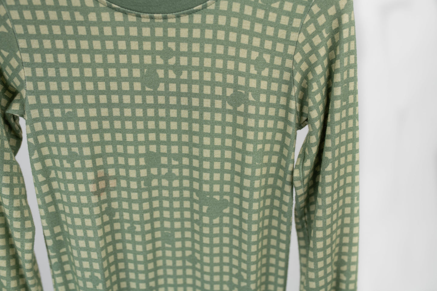 Close-up of sage green baby romper fabric with a subtle tan grid pattern and hidden tactical icons like pineapples, rifles, and helmets, designed by 3rd Coast Limited.