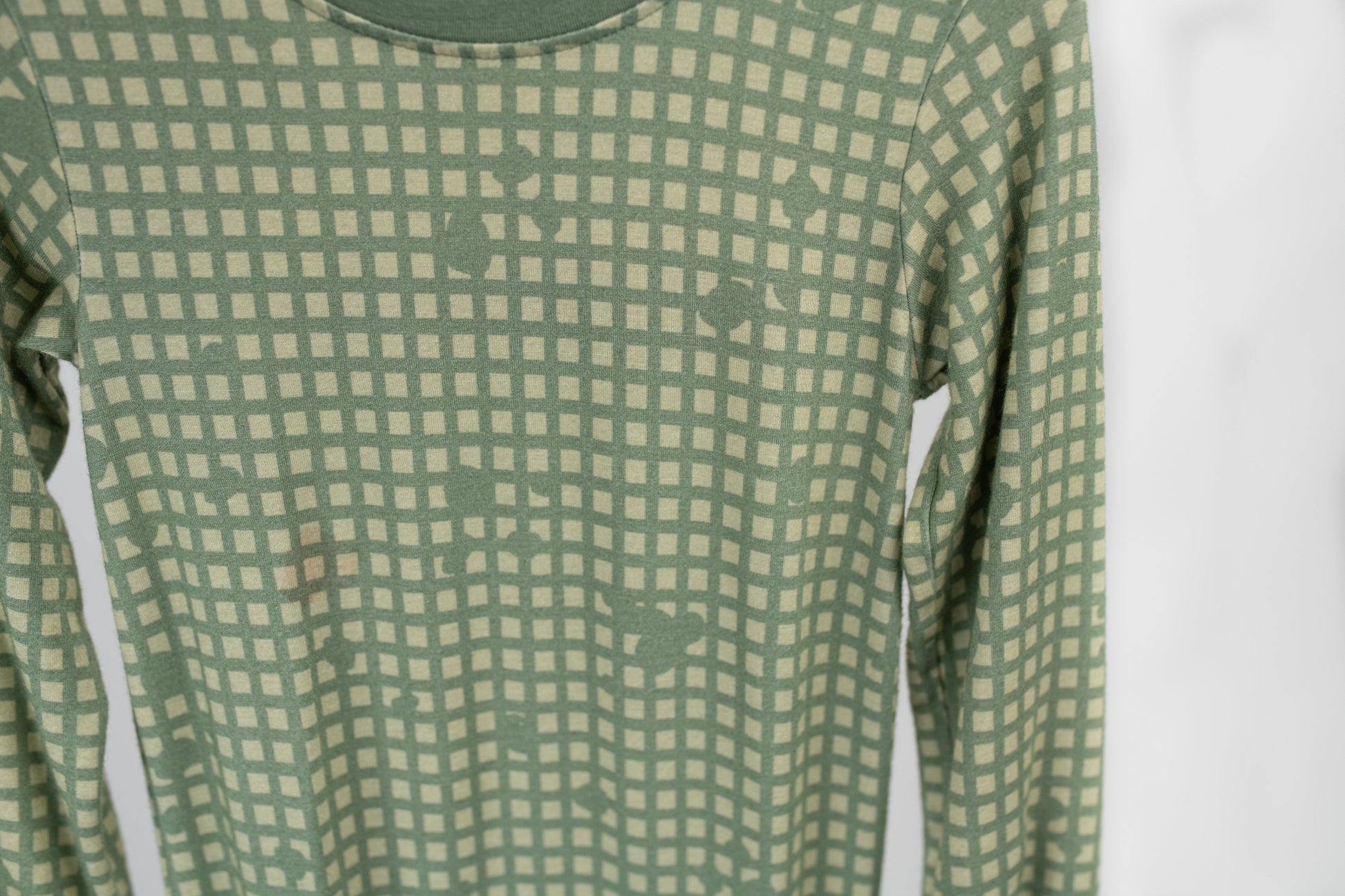 Close-up of sage green baby romper fabric with a subtle tan grid pattern and hidden tactical icons like pineapples, rifles, and helmets, designed by 3rd Coast Limited.