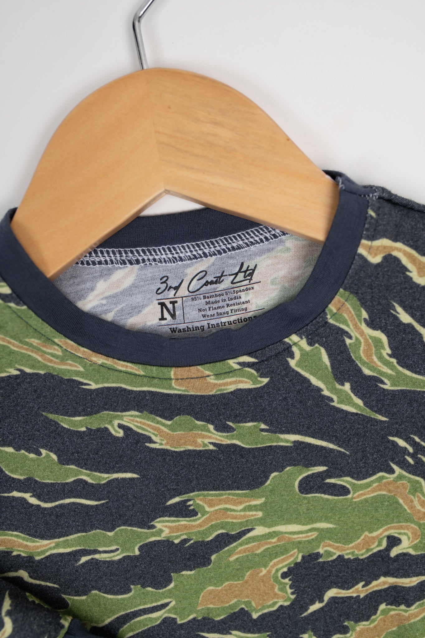 Close-up of a camo baby romper by 3rd Coast Limited, showing the green and brown tiger stripe pattern with navy trim and the inner neck label reading ‘95% Bamboo 5% Spandex – Made in India.