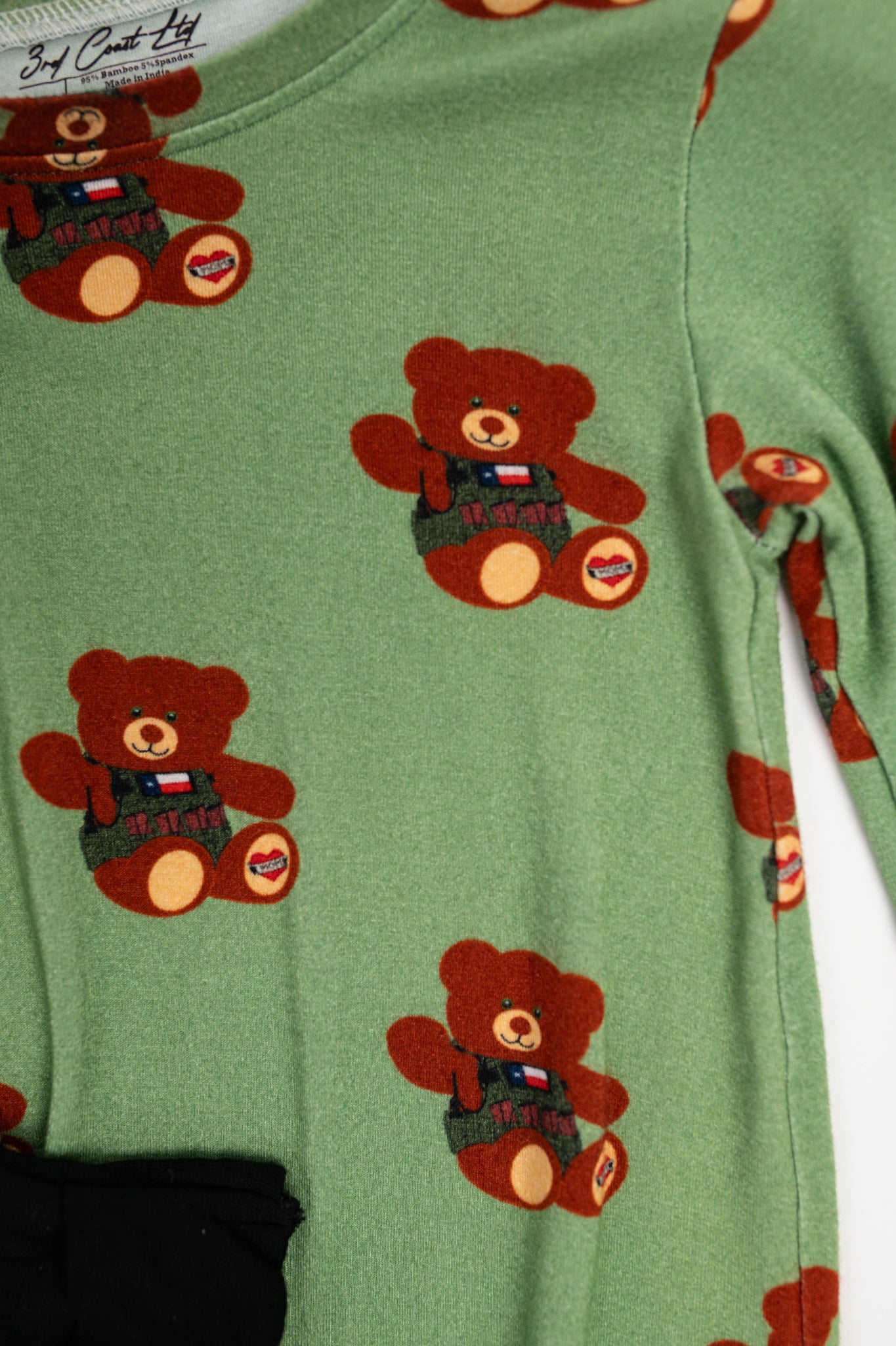 Close-up of green baby romper fabric featuring a repeating print of a brown tactical teddy bear wearing a vest with a Texas flag patch and a heart-shaped ‘Mom’ tattoo on its foot.