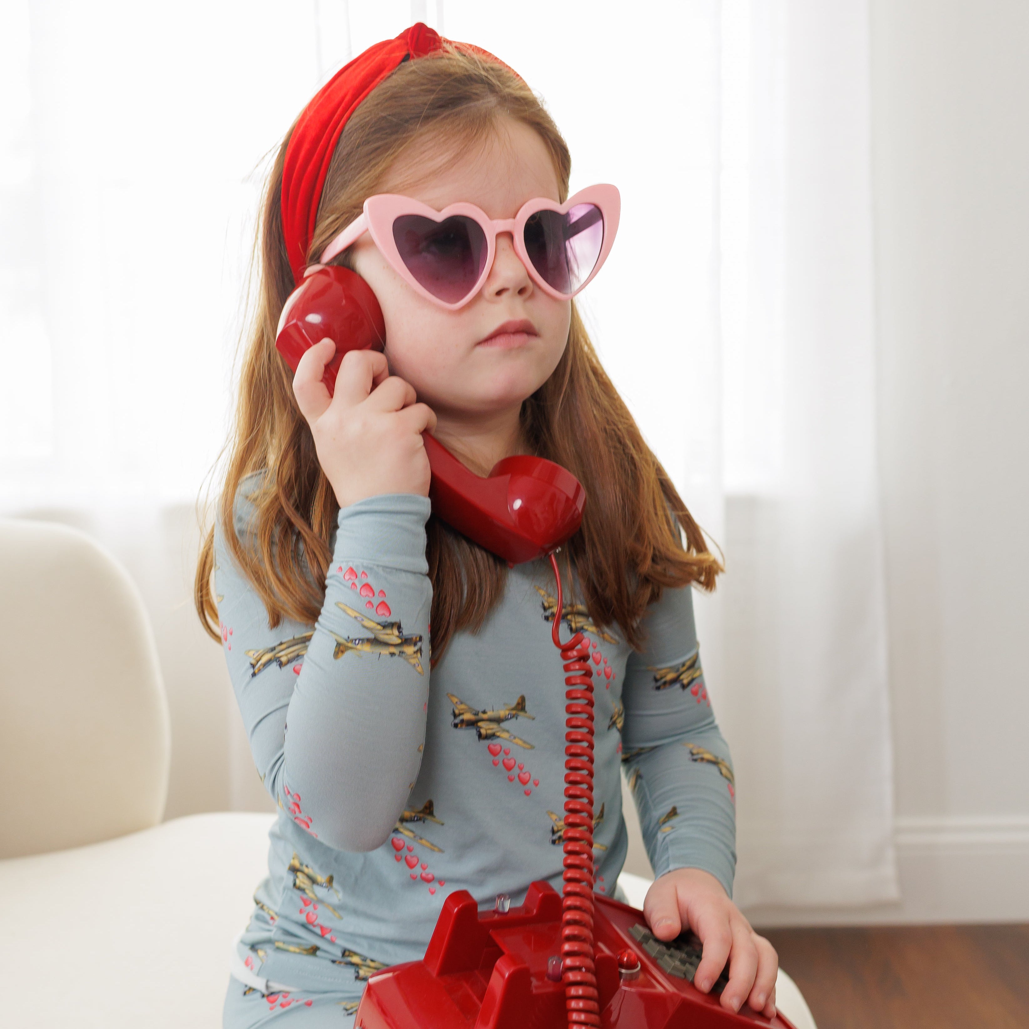 Child playing with a red phone wearing heart-shaped sunglasses and a red headband.