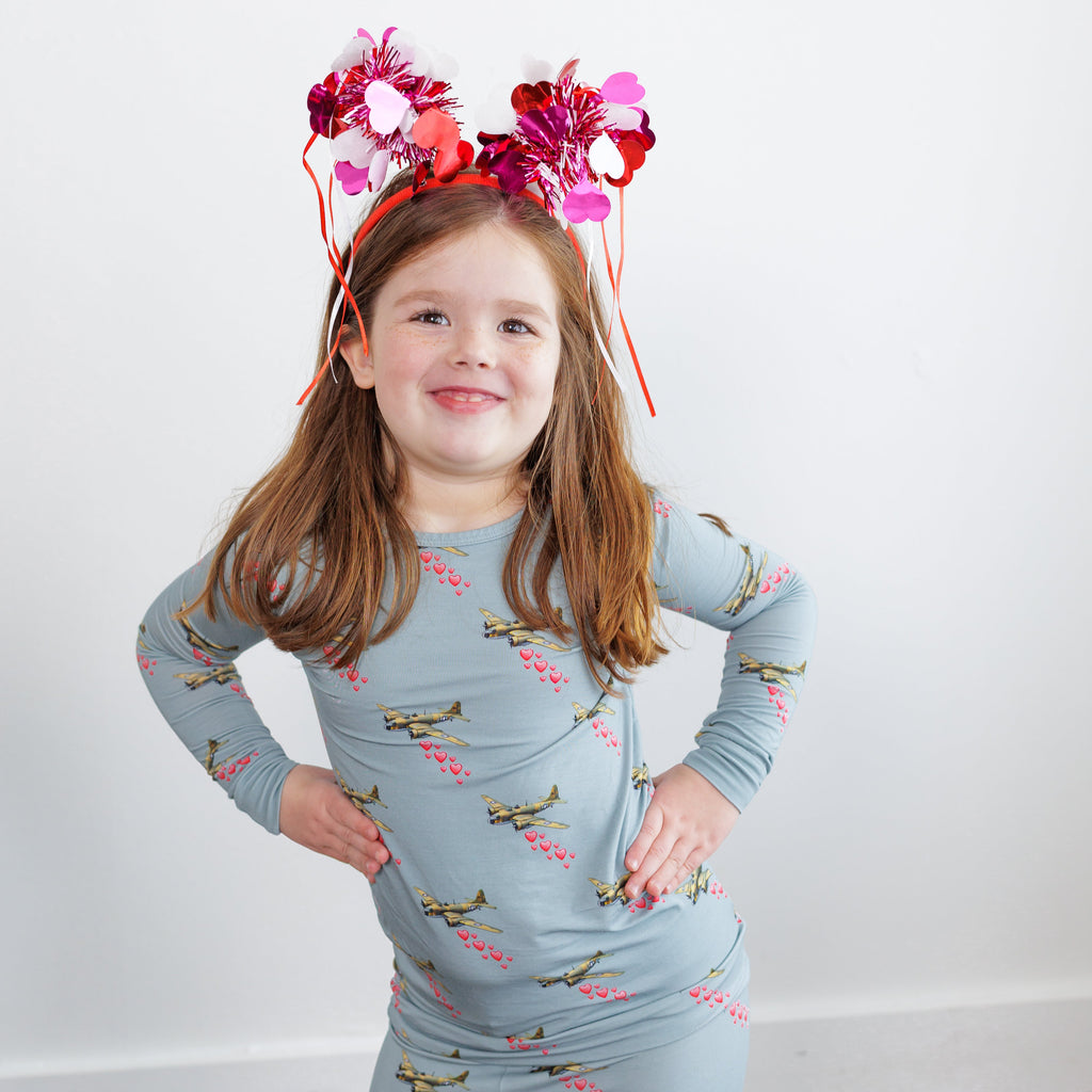 Young girl wearing a blue pajama set with airplane pattern and pink headband with flowers on a white background.