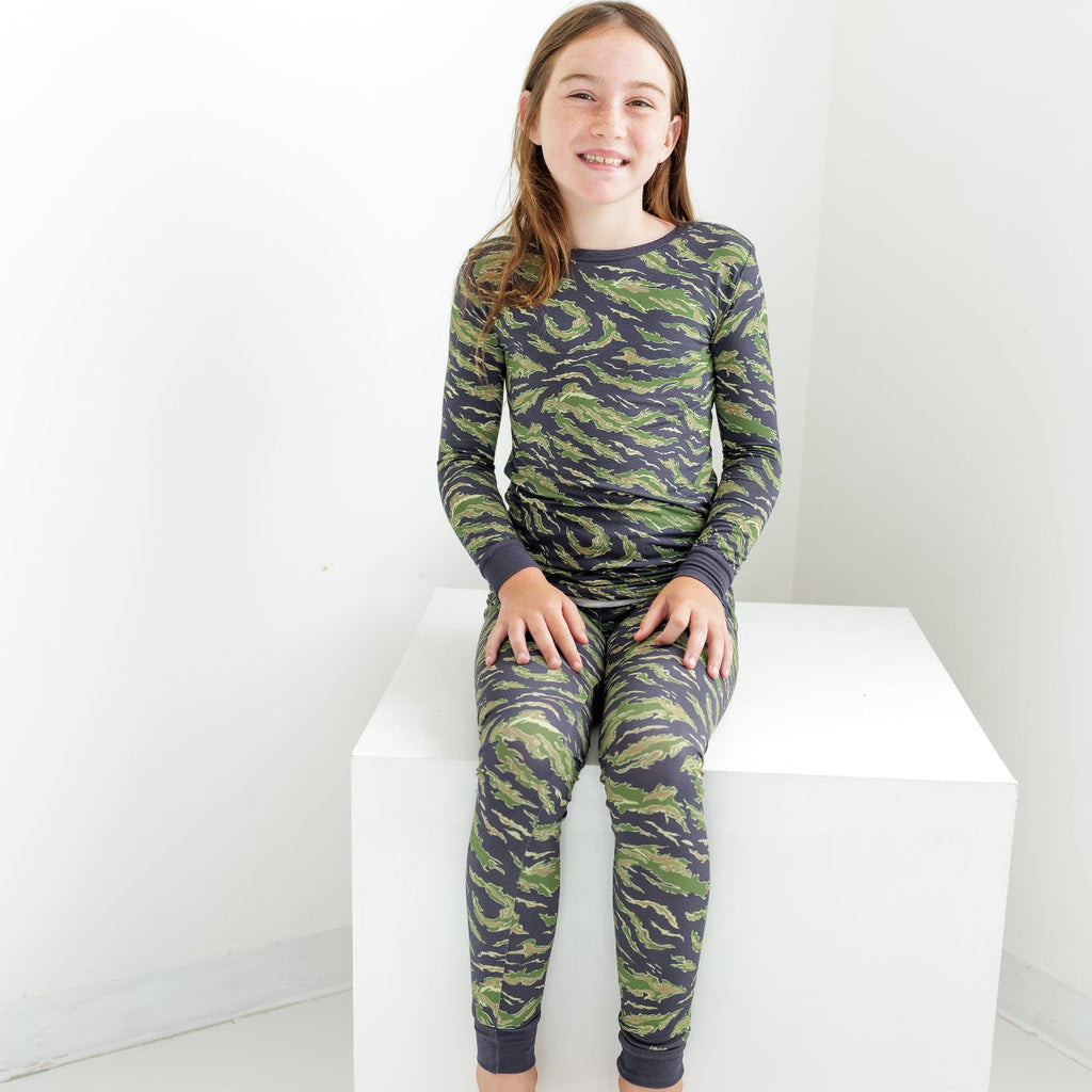 Child wearing green camouflage pajamas sitting on a white box against a white background