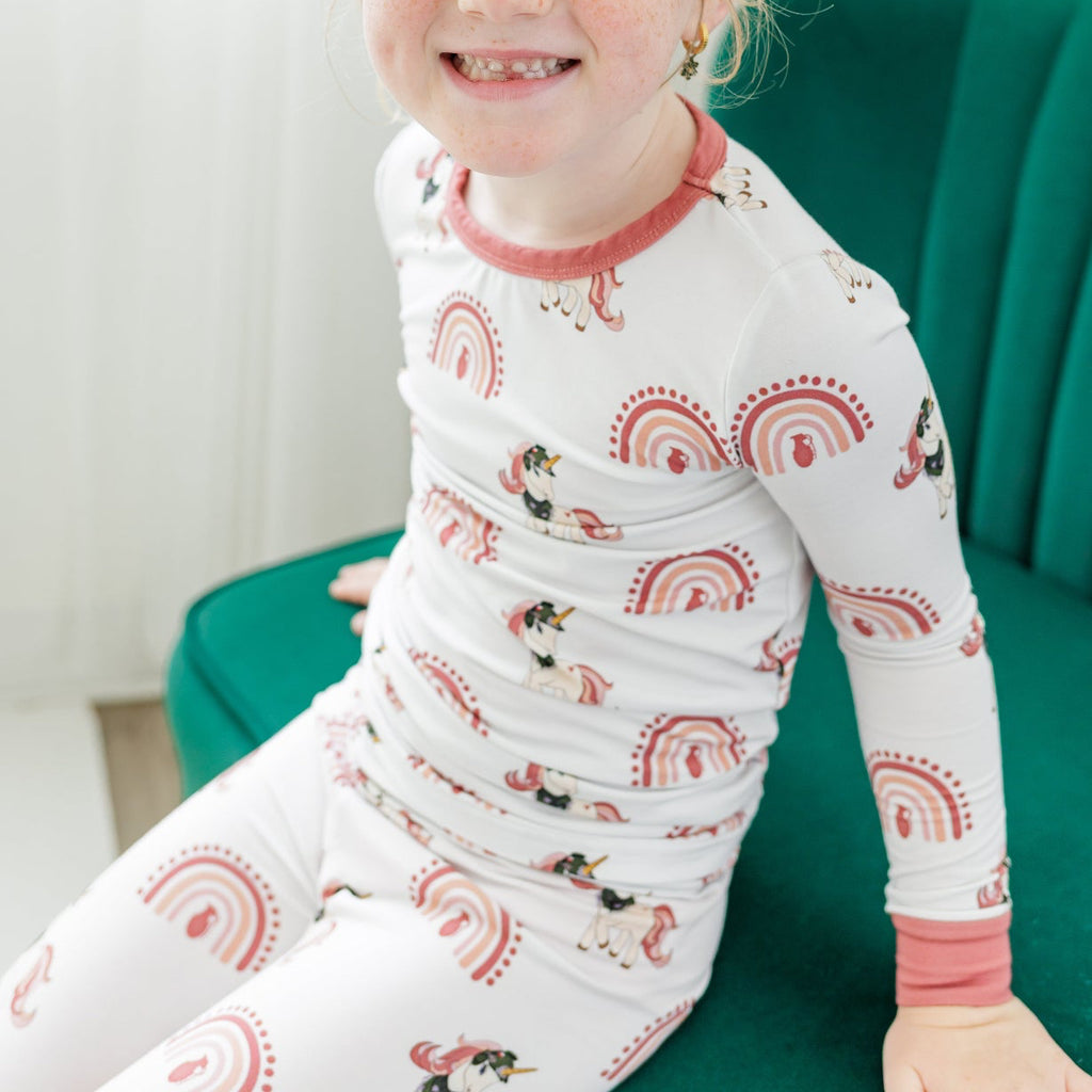 Child wearing pajamas with a pattern of owls, rainbows, and stars, sitting on a green chair.