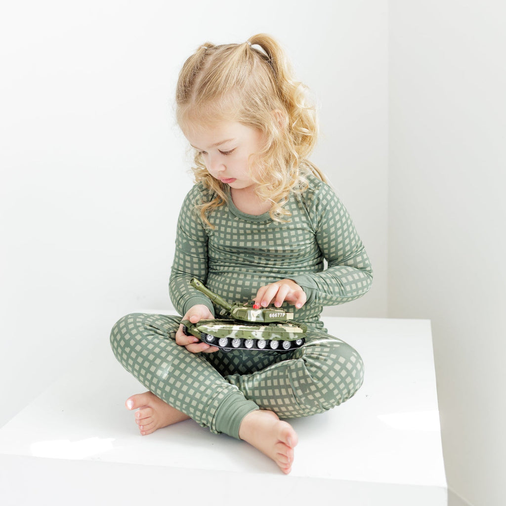 Child wearing green pajamas sitting on a white surface with a white background