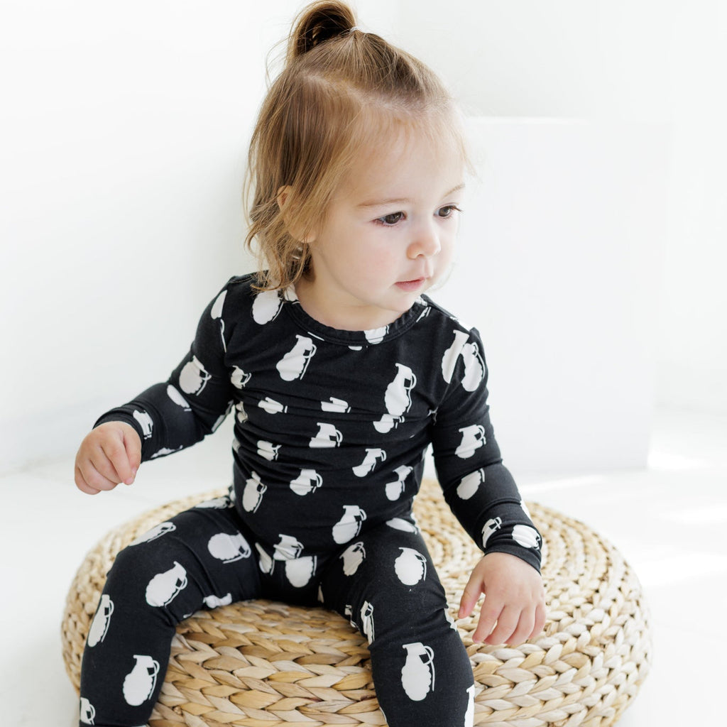 Child wearing a black outfit with white patterns sitting on a woven stool against a white background