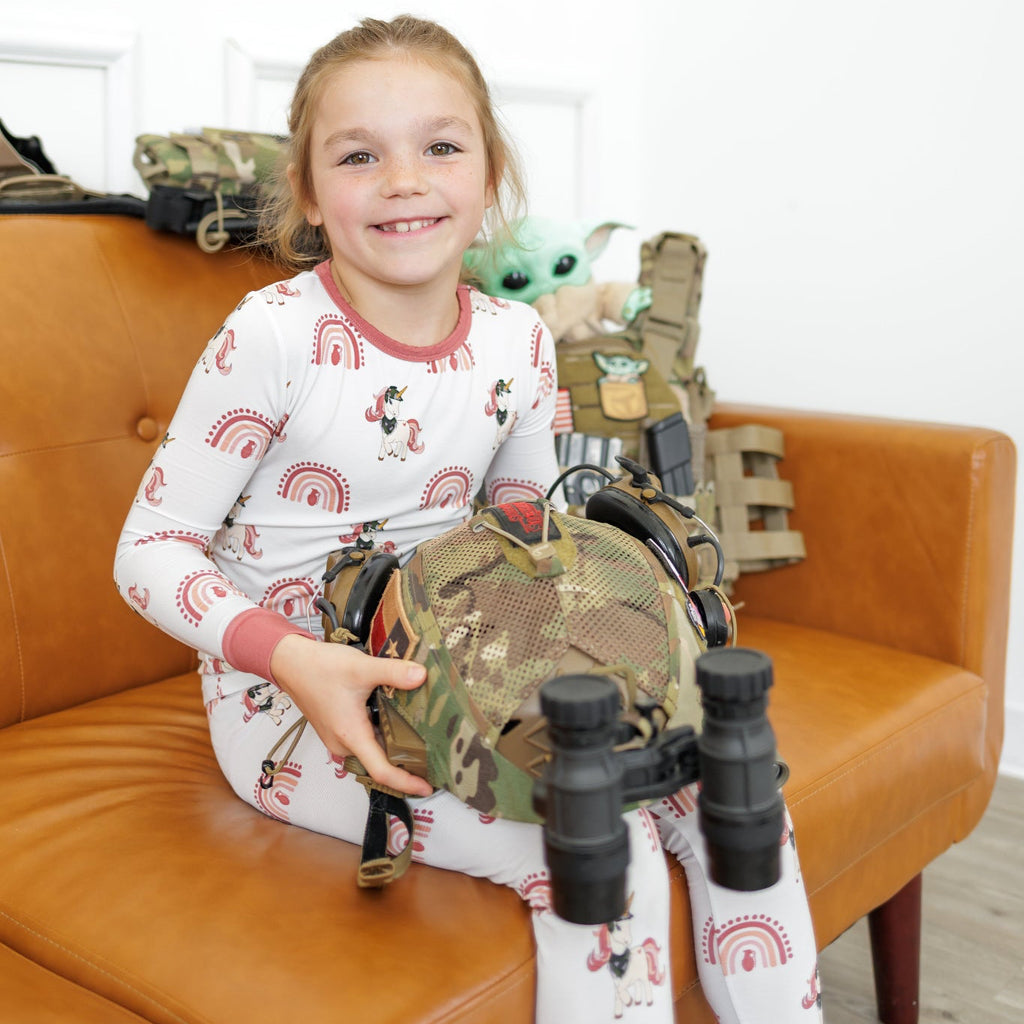 Child in pajamas holding a toy gun and helmet on a brown couch with toys in the background.
