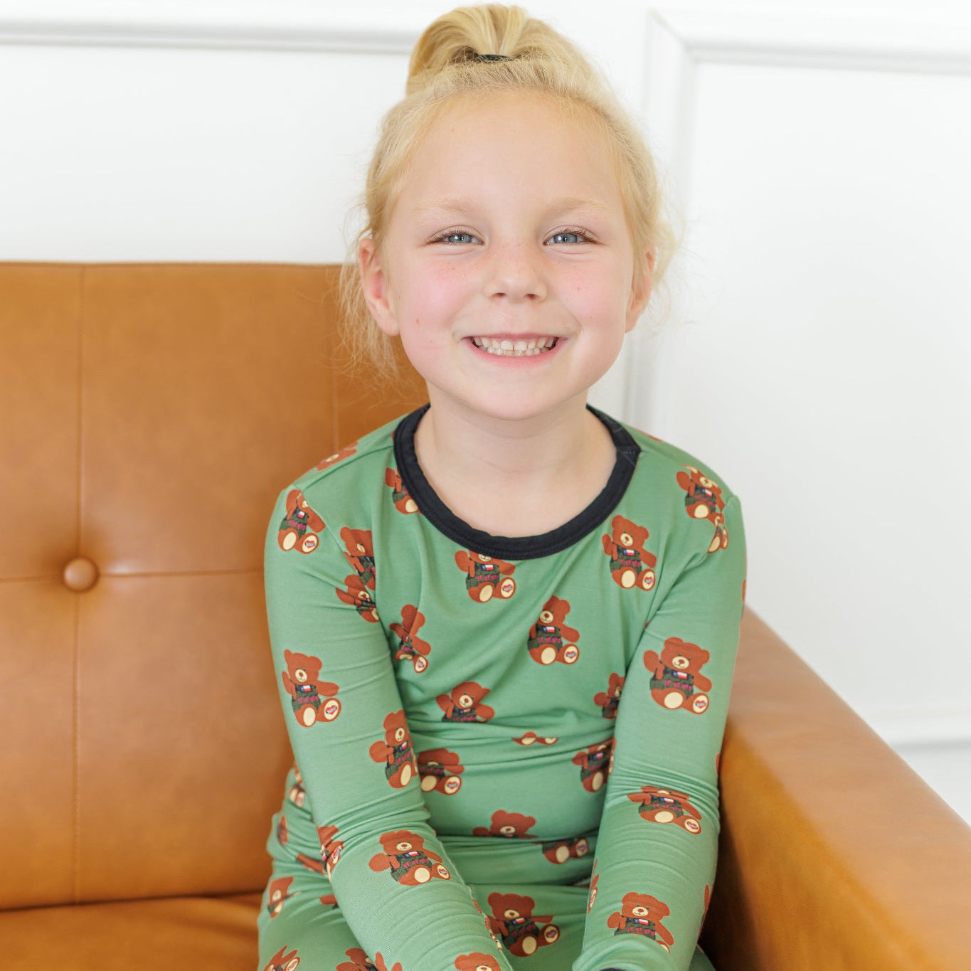 Young girl wearing green pajamas with floral patterns sitting on a brown couch.