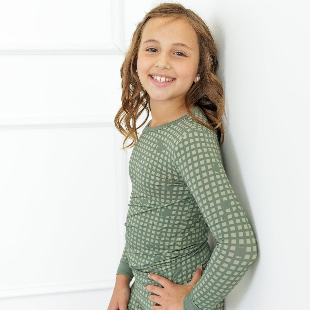 Young girl wearing a green patterned outfit against a white wall