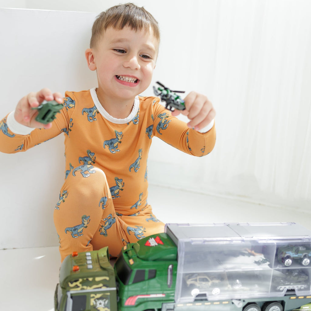 Child in orange pajamas with dinosaur pattern playing with a toy truck on a white background