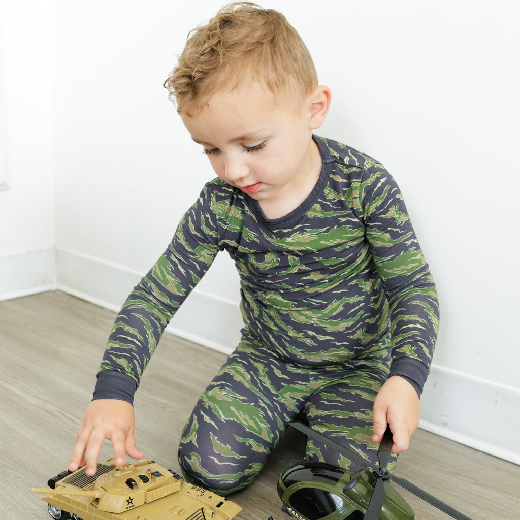 Child playing with toy tank and helicopter on a wooden floor.