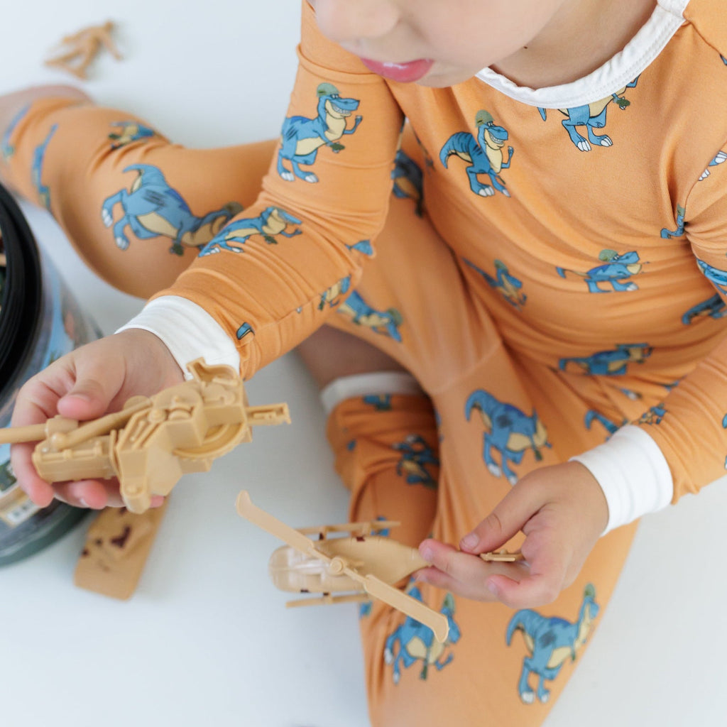 Child in orange dinosaur pajamas playing with wooden toys on a white floor.