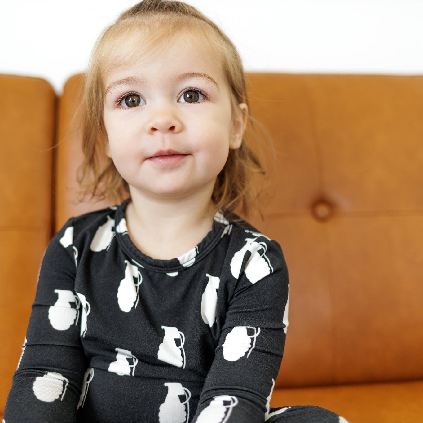 Child wearing a black outfit with white patterns sitting on a brown couch.