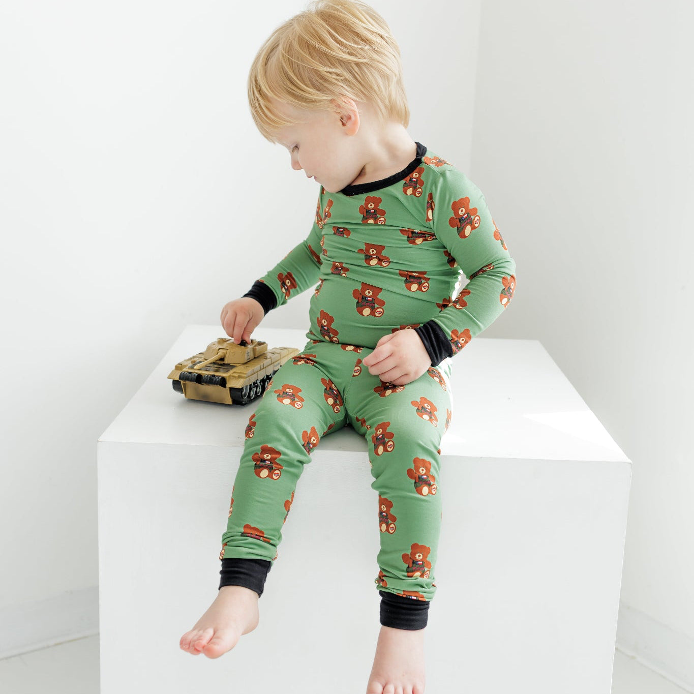 Child wearing green pajamas with a pattern, sitting on a white surface.