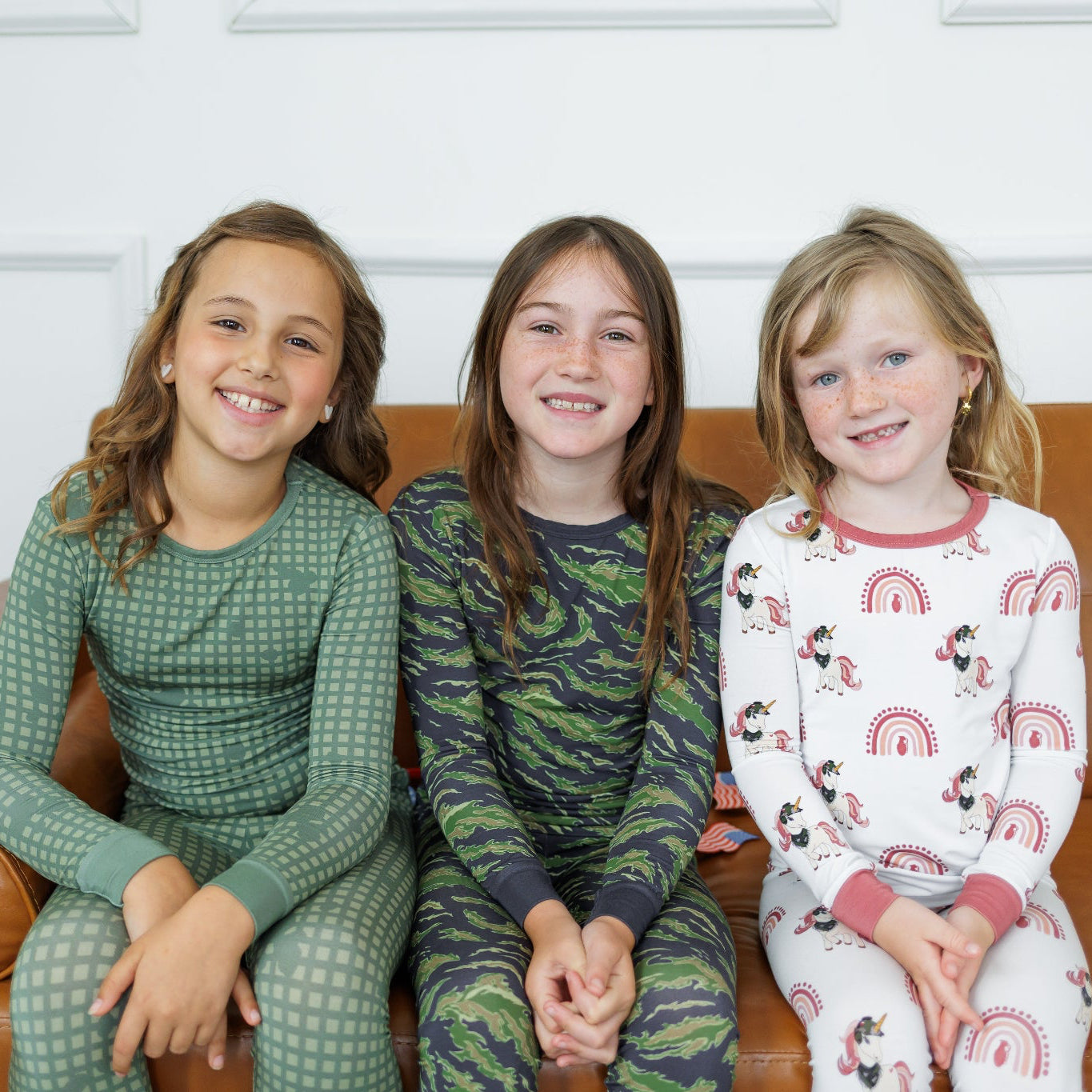 Three children sitting on a brown couch wearing pajamas.