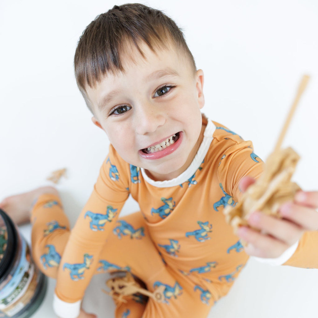 Child in orange pajama with animal pattern holding a toy airplane on a white background