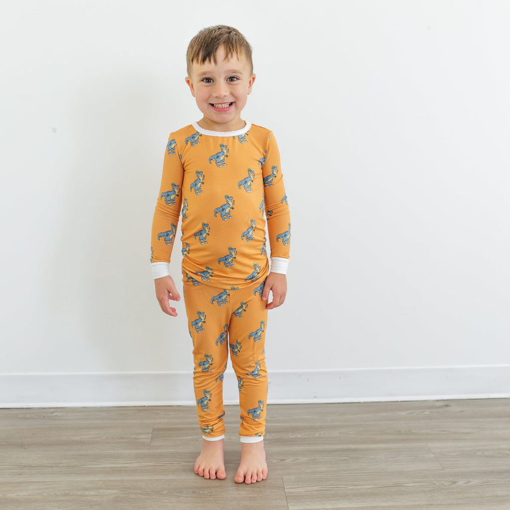 Child wearing orange dinosaur-patterned pajamas standing on a wooden floor with a white wall background