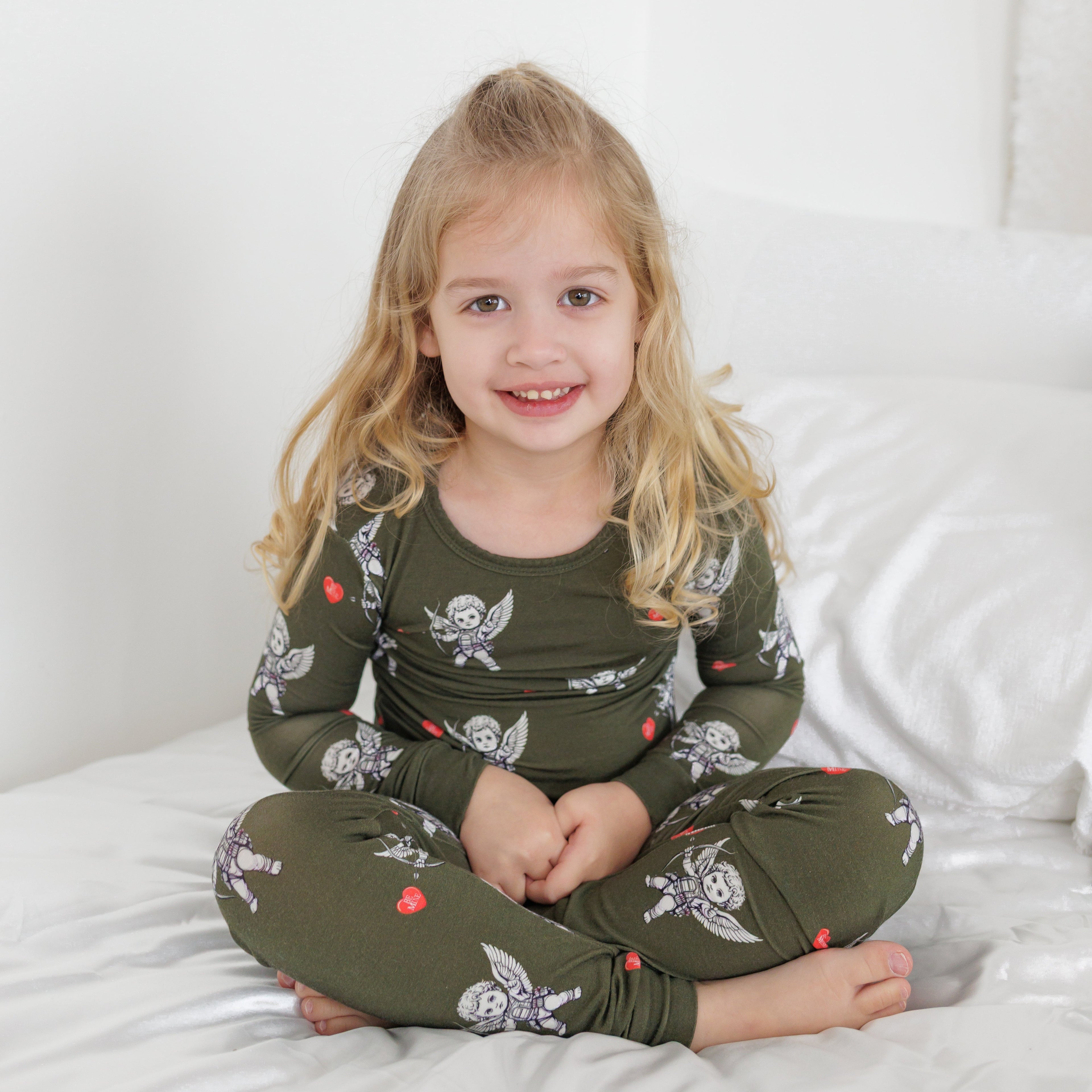 Child wearing green pajamas with skull and crossbones pattern on a white bed.