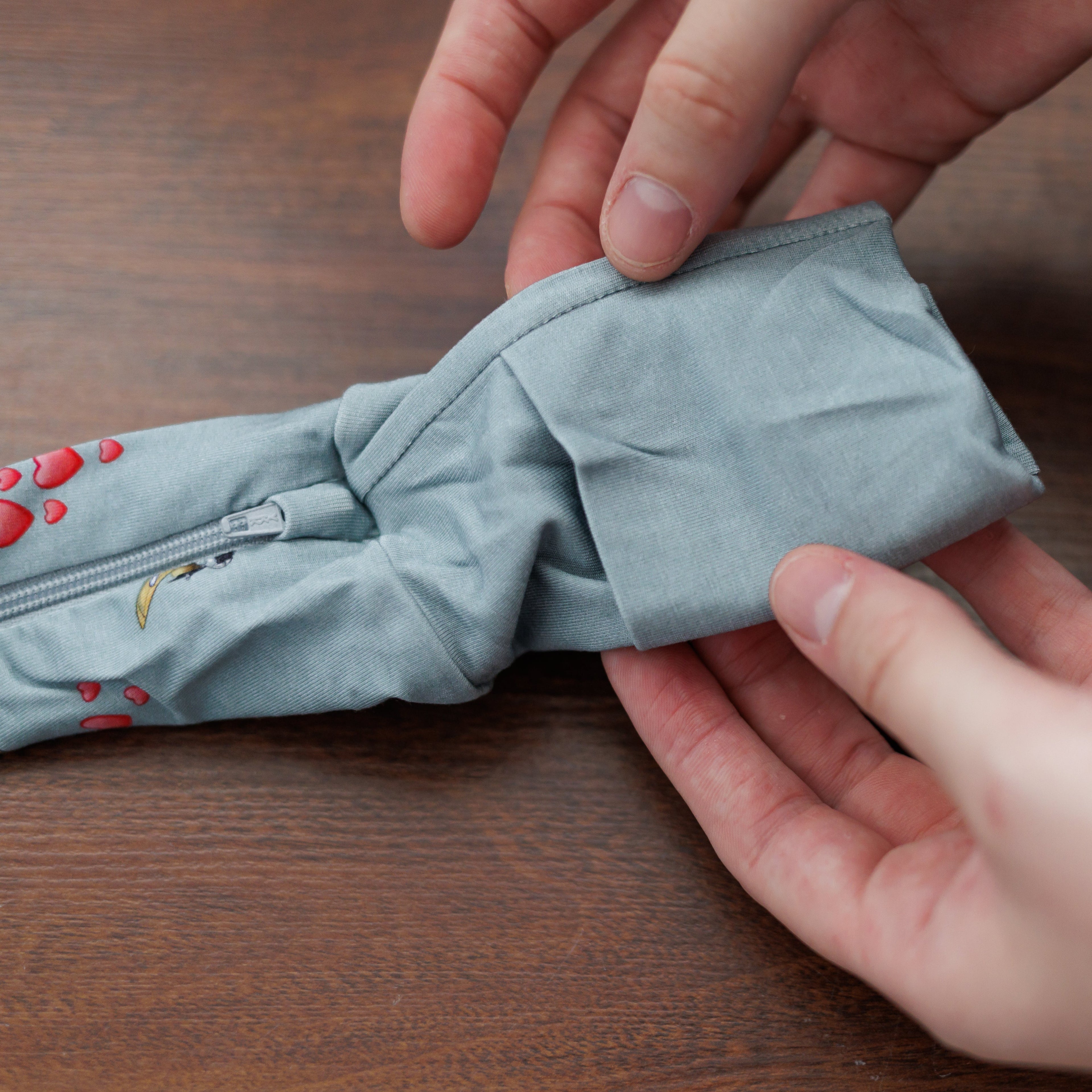 Person folding a light blue jacket on a wooden surface