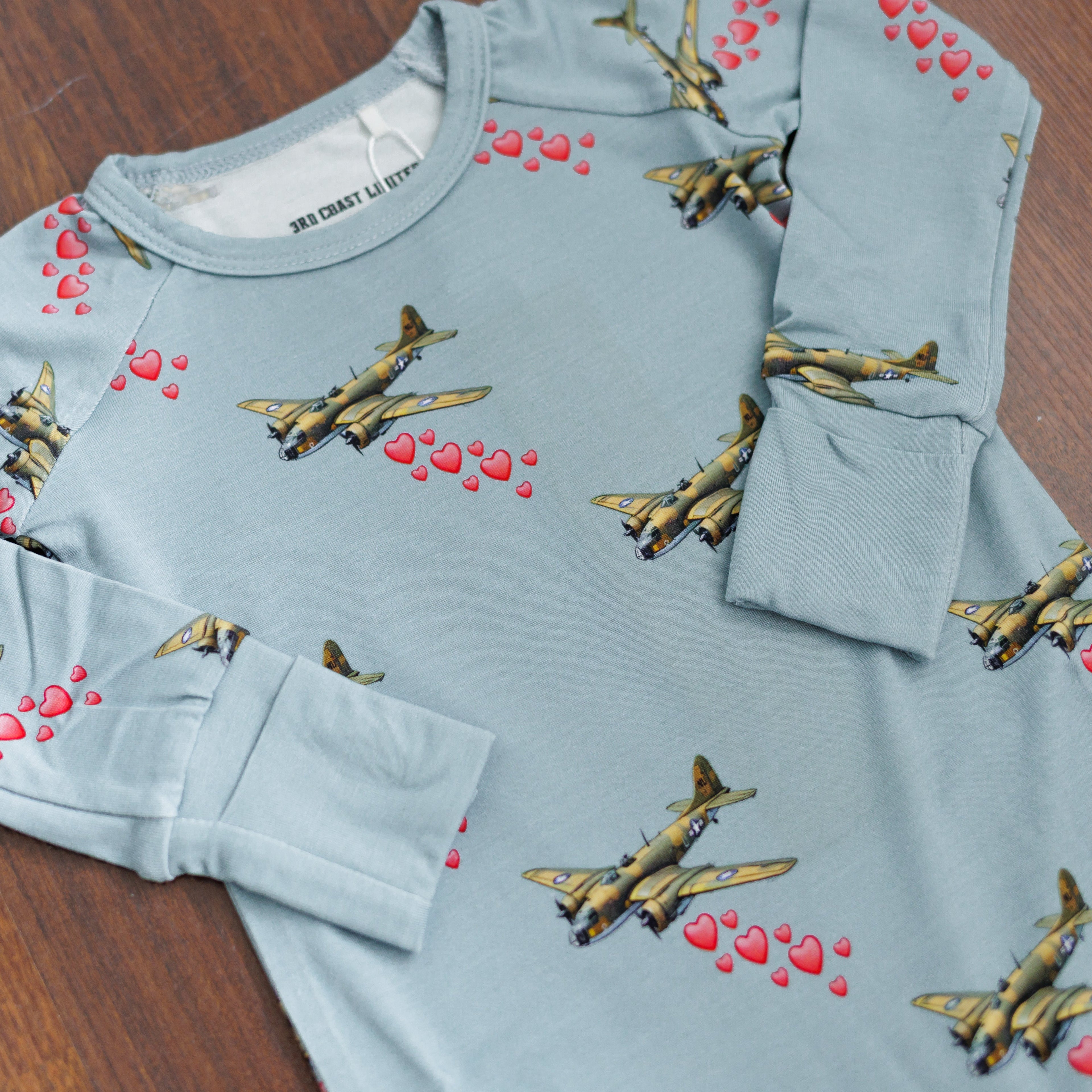 Light blue sweatshirt with airplane and heart patterns on a wooden surface