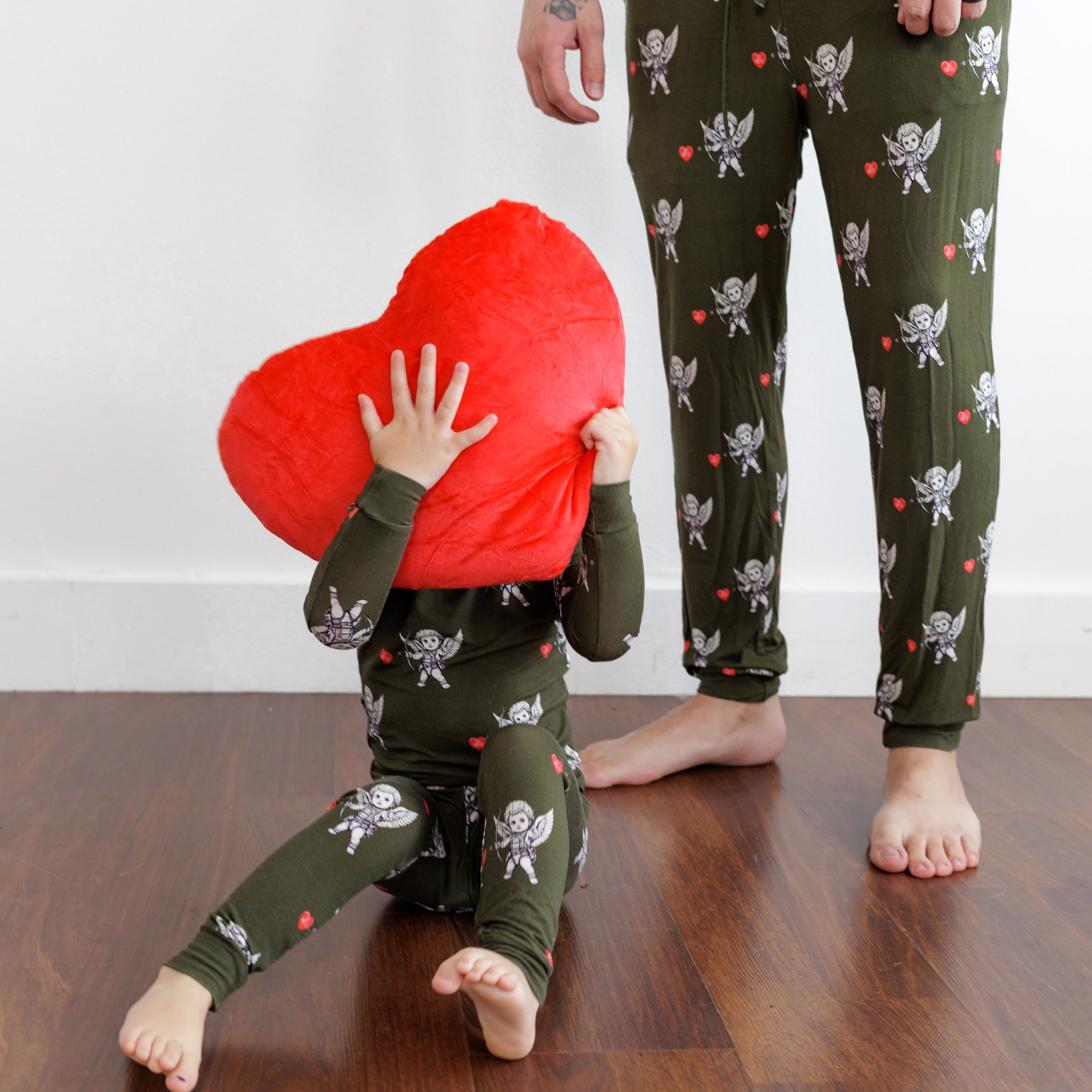 Two people wearing matching pajama sets with a heart-shaped pillow on a wooden floor.