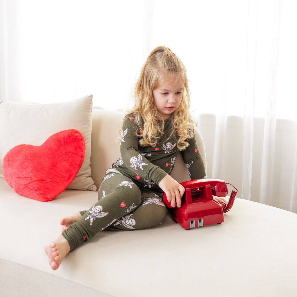 Child playing with a red toy phone on a white couch with a heart-shaped pillow.