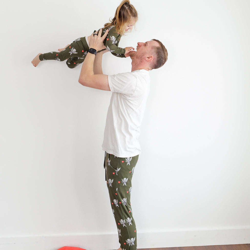 Man lifting a child in a room with a white wall and wooden floor.