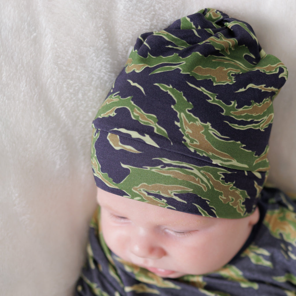 Baby swaddled in a green and blue camouflage pattern on a white blanket