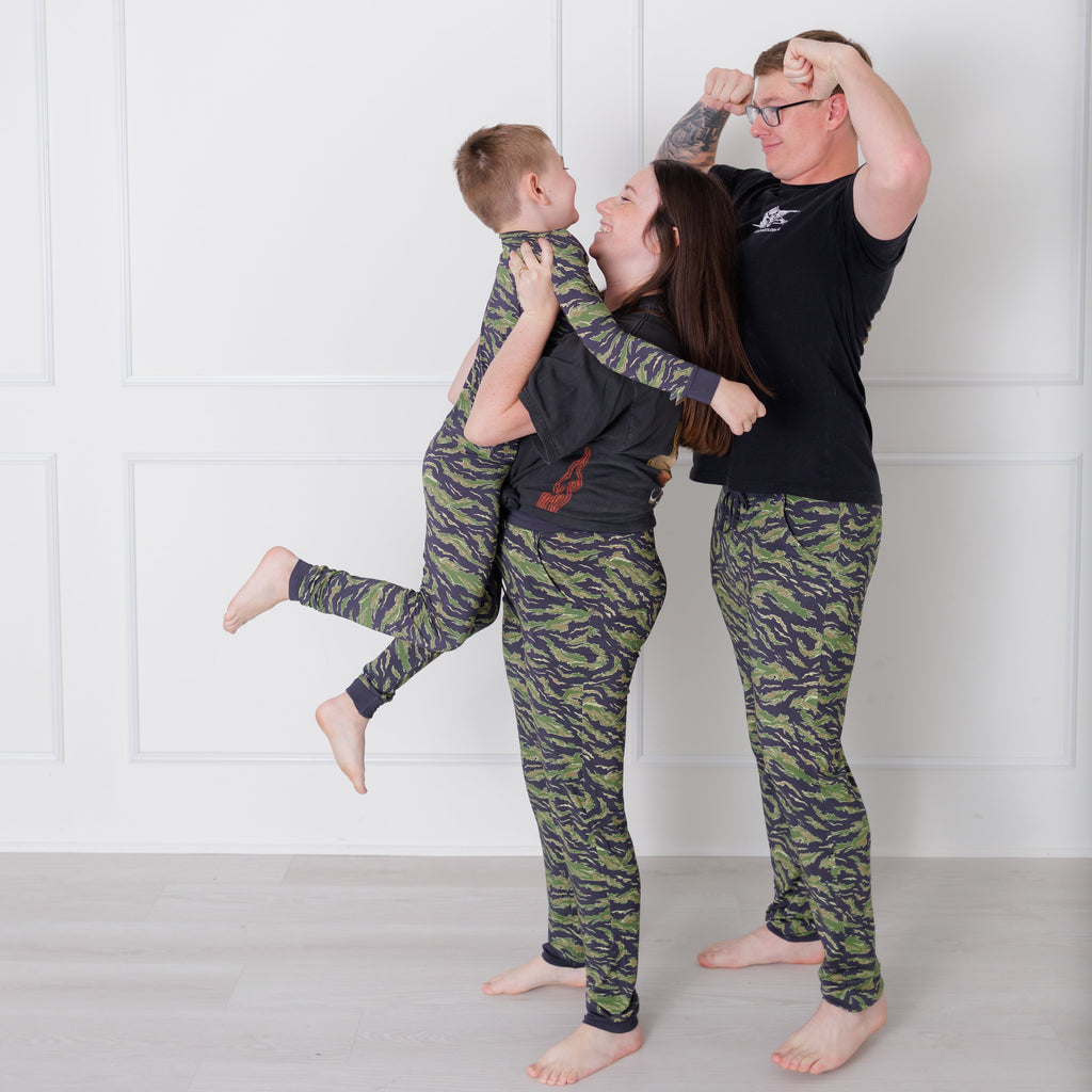 Two people in matching camouflage pajama sets against a white wall.