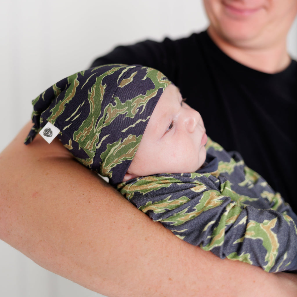 Person holding a baby wrapped in a green and blue patterned blanket against a white background