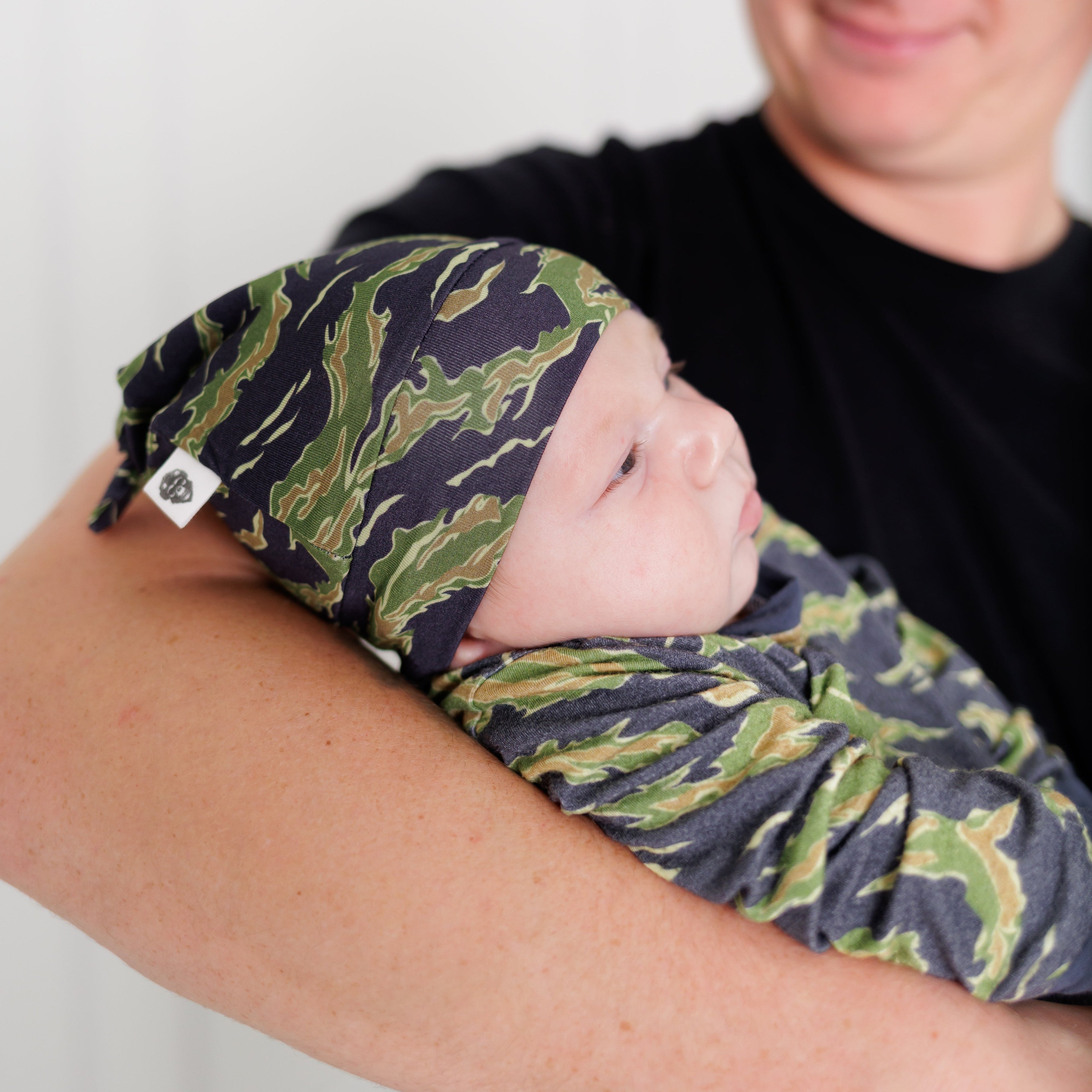 Person holding a baby wrapped in a green and blue patterned blanket against a white background