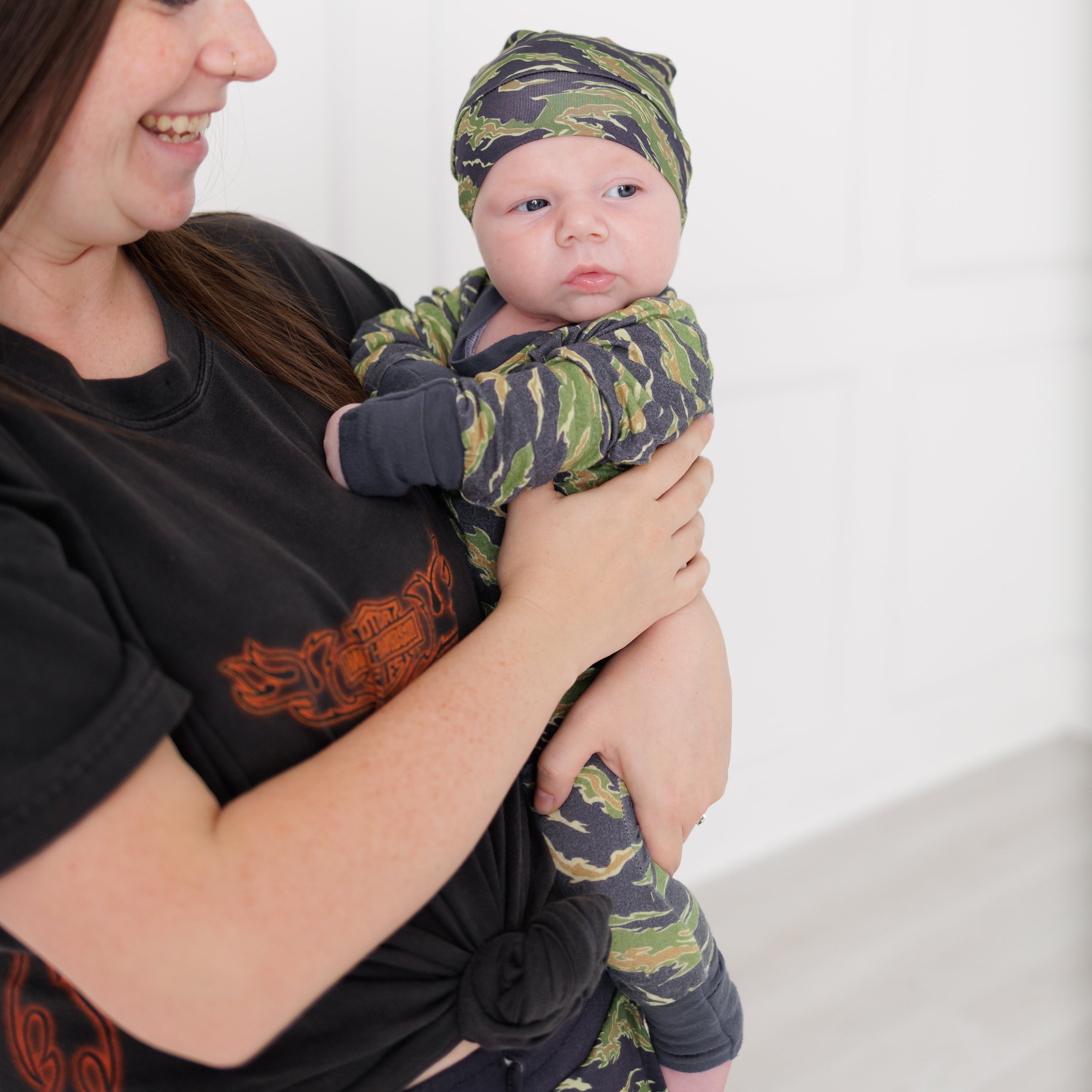 Woman holding a baby dressed in camouflage clothing and hat against a white background