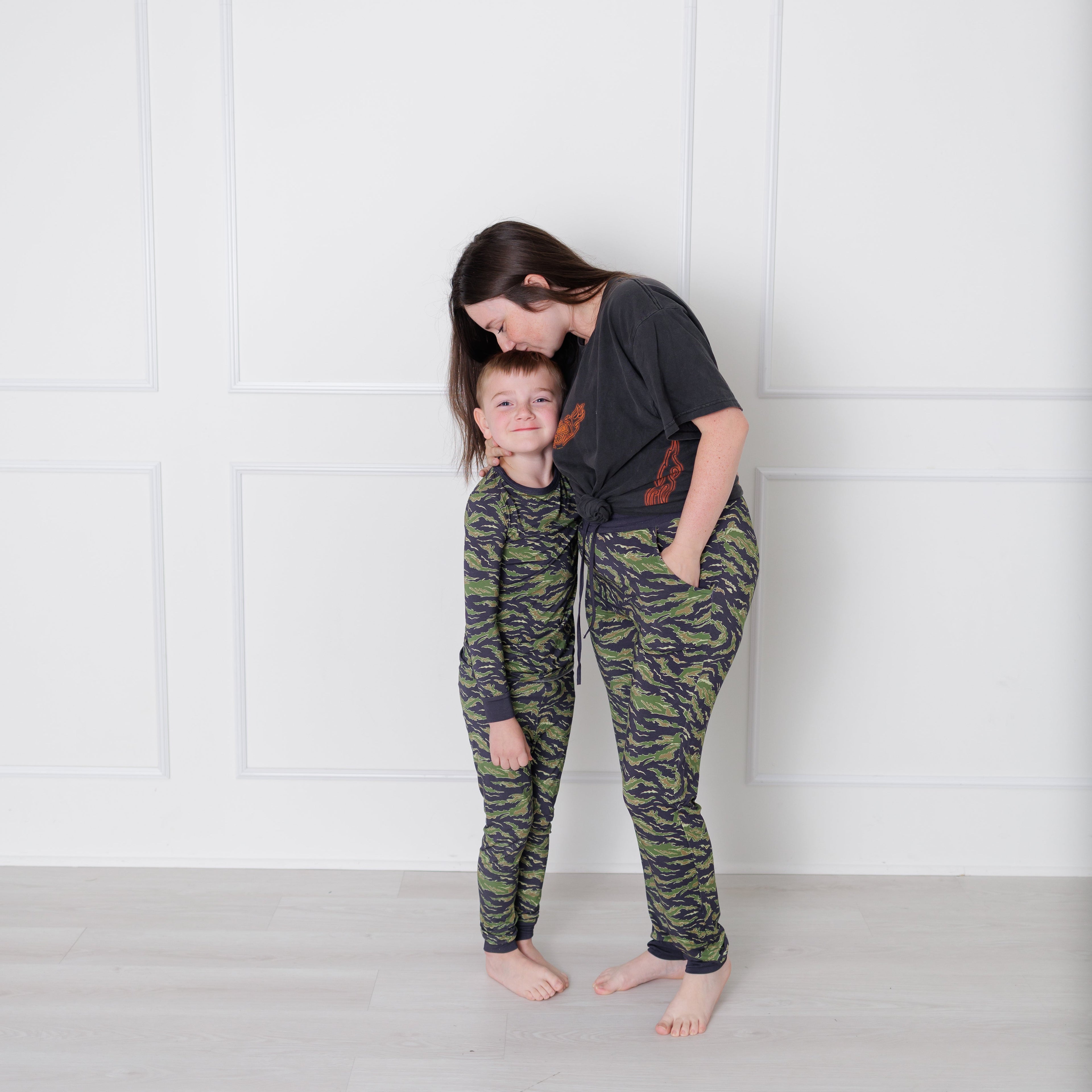 Two people wearing camouflage pajamas standing against a white wall.