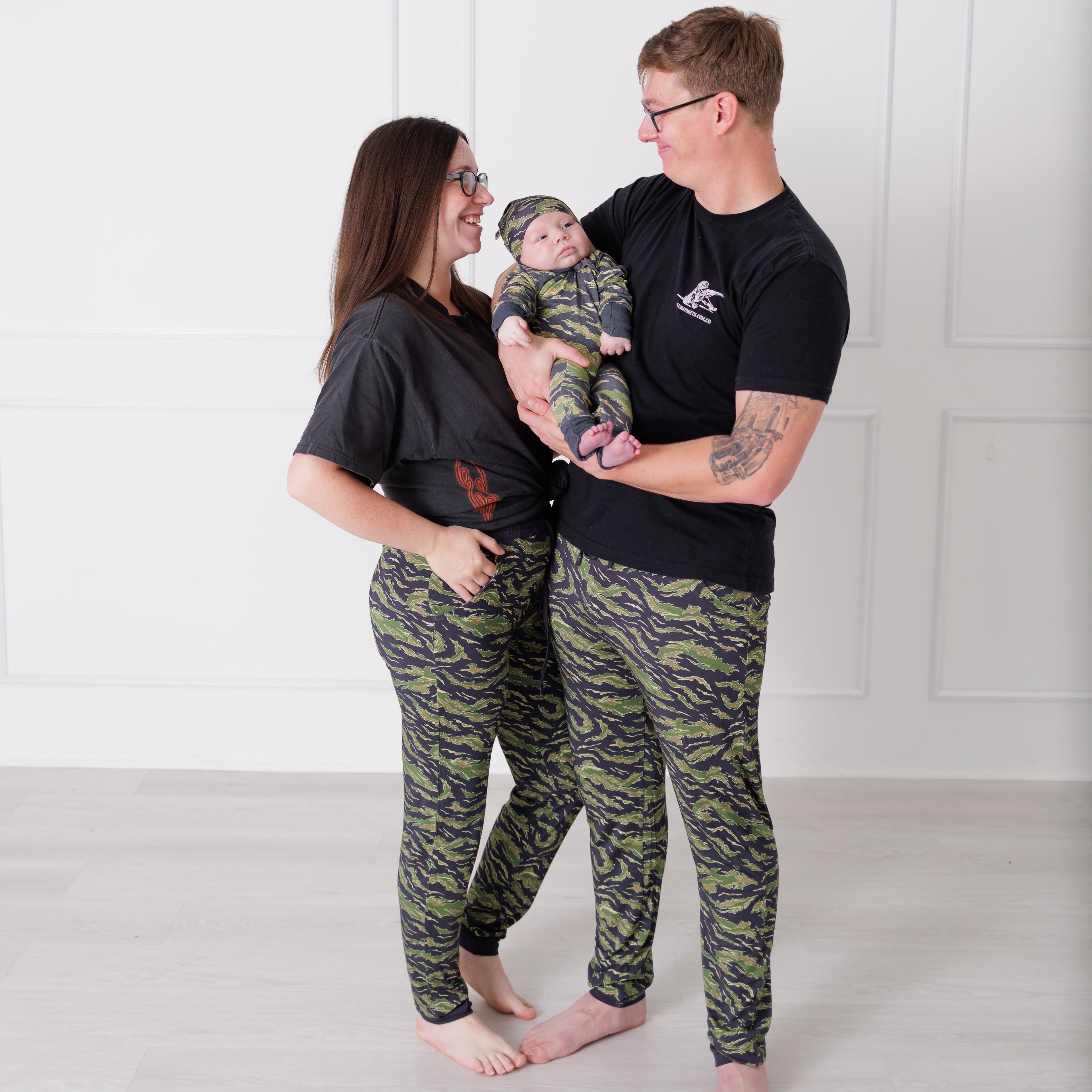Family of three wearing matching camouflage outfits against a white background
