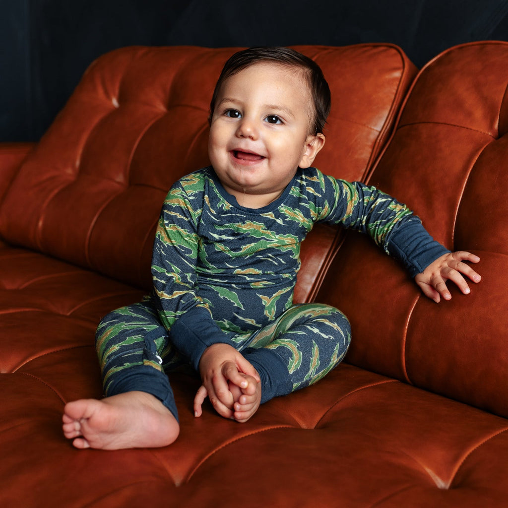 Child wearing a blue and green patterned onesie sitting on a leather couch against a dark background